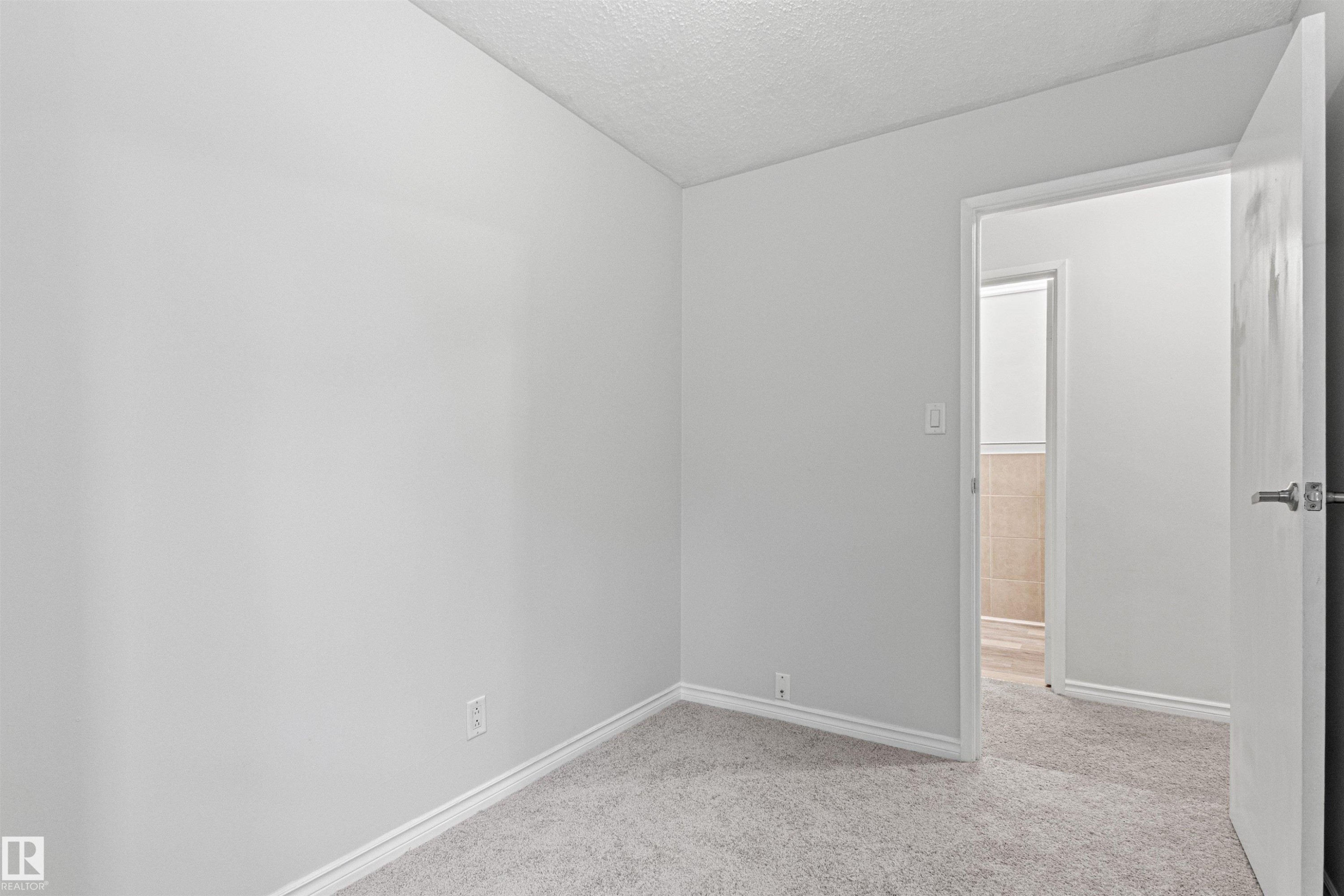 Bright secondary bedroom featuring neutral wall finishes, plush carpeting, and direct access to adjoining spaces through solid-core doors - #9 14230 80 St Nw, Edmonton, AB - Indoor Photo Showing Other Room