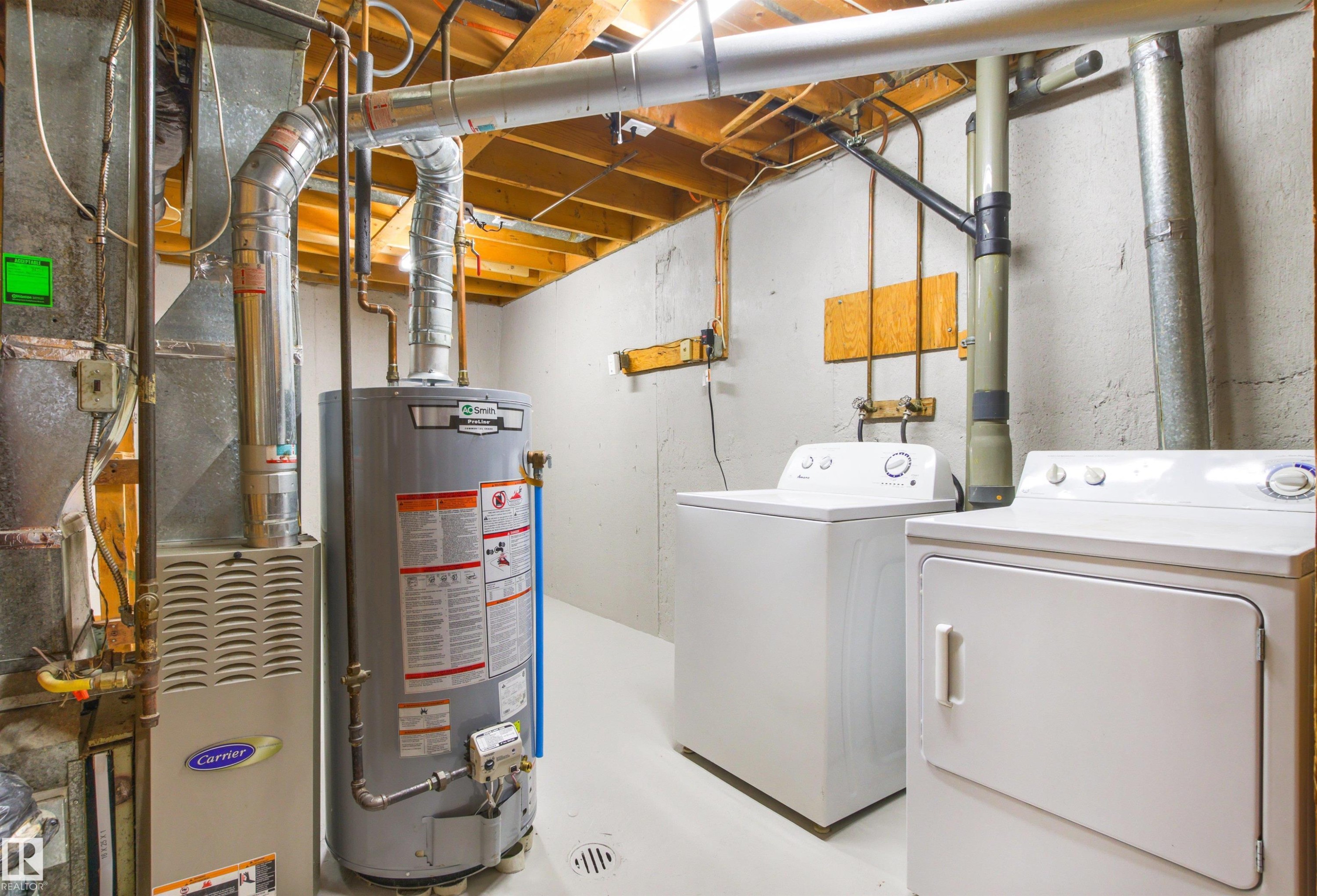 Utility room featuring a gas water heater with insulated piping, electric dryer, front-load washing machine, and exposed beam ceiling with yellow-painted wood trusses - #9 14230 80 St Nw, Edmonton, AB - Indoor Photo Showing Basement