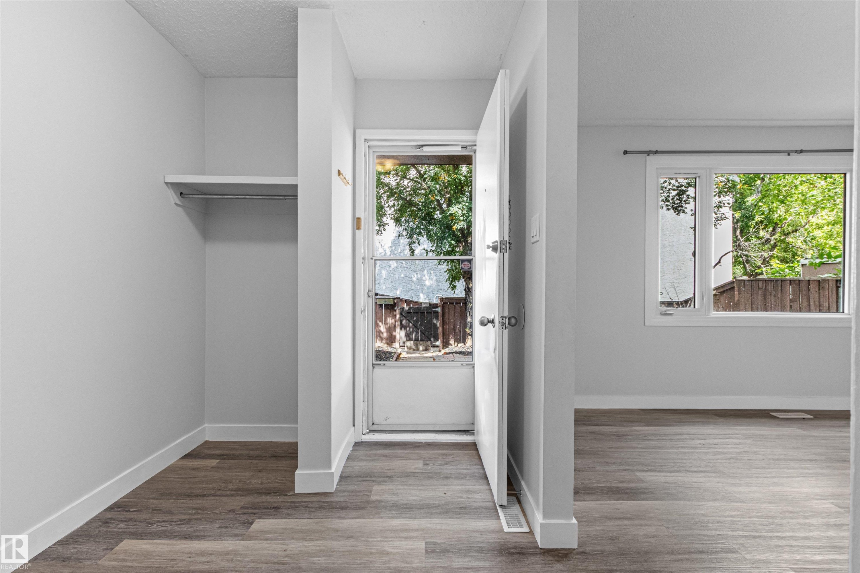 Wood-finish flooring, white walls, built-in closet shelving and rod, white trim, and a prominent window - #9 14230 80 St Nw, Edmonton, AB - Indoor Photo Showing Other Room