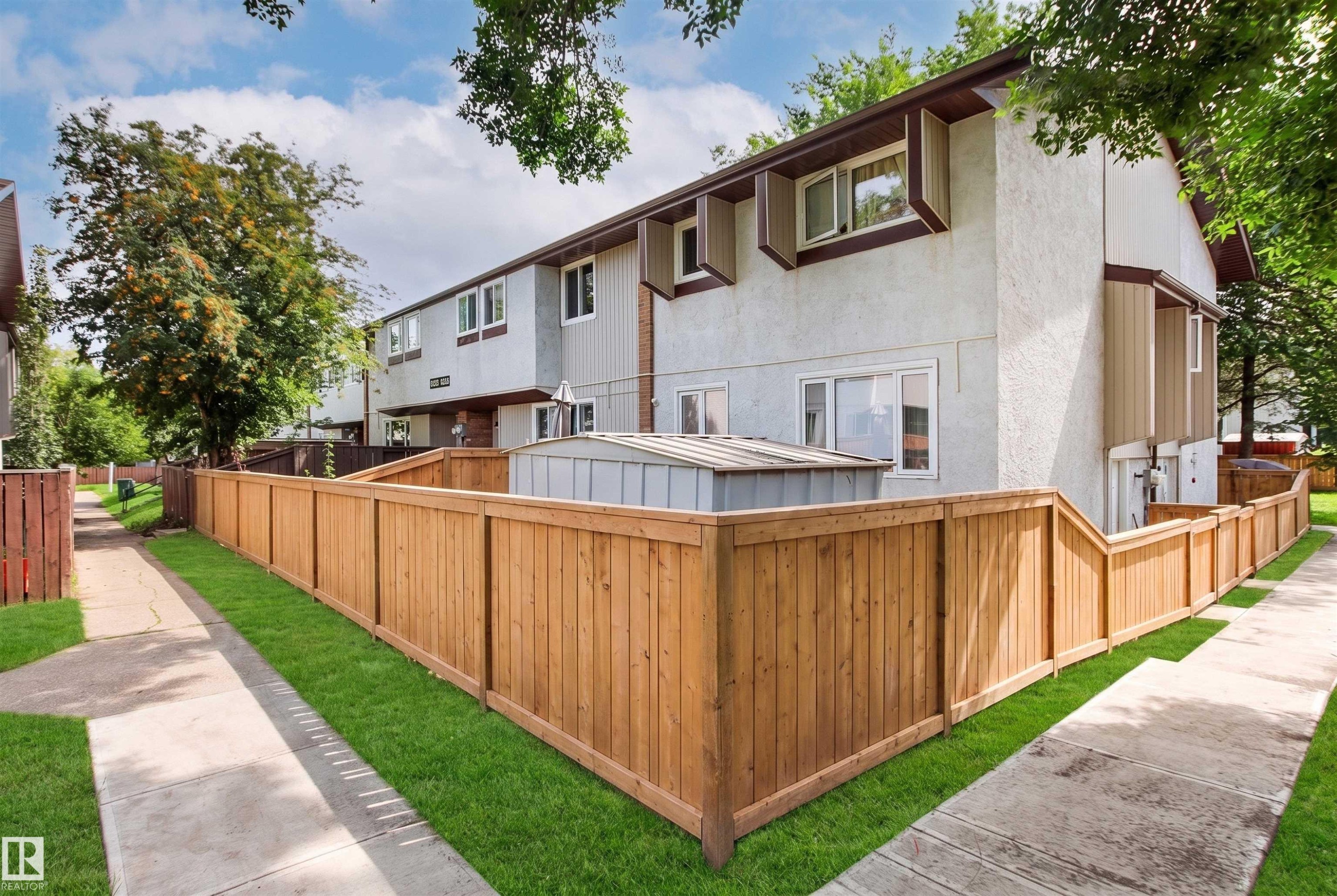 Spacious backyard featuring a newly constructed wood-finish privacy fence, manicured lawn, and mature landscaping - #9 14230 80 St Nw, Edmonton, AB - Outdoor With Exterior
