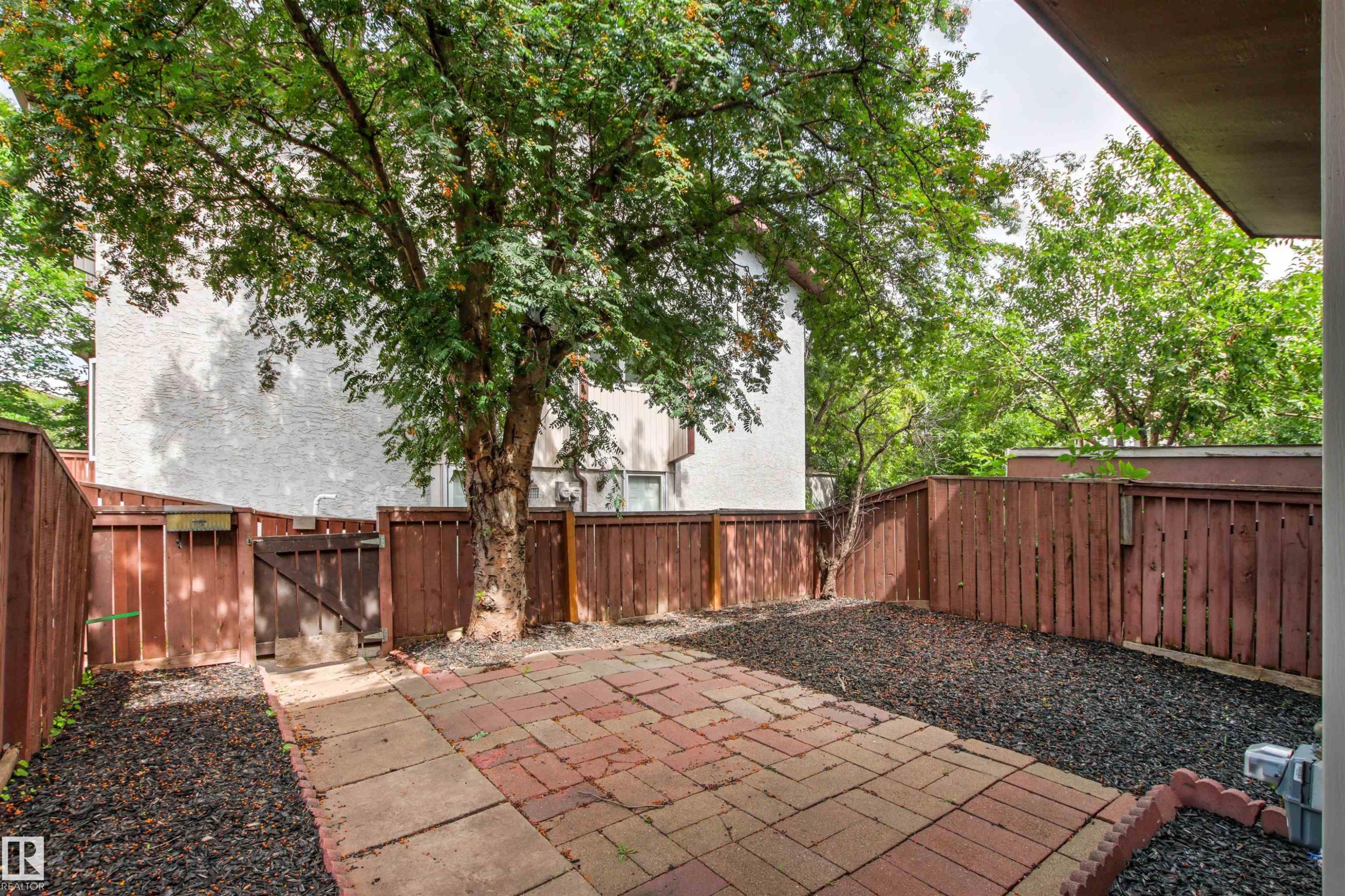 Private outdoor patio featuring brick pavers, dark aggregate landscaping, and a wood privacy fence - #9 14230 80 St Nw, Edmonton, AB - Outdoor