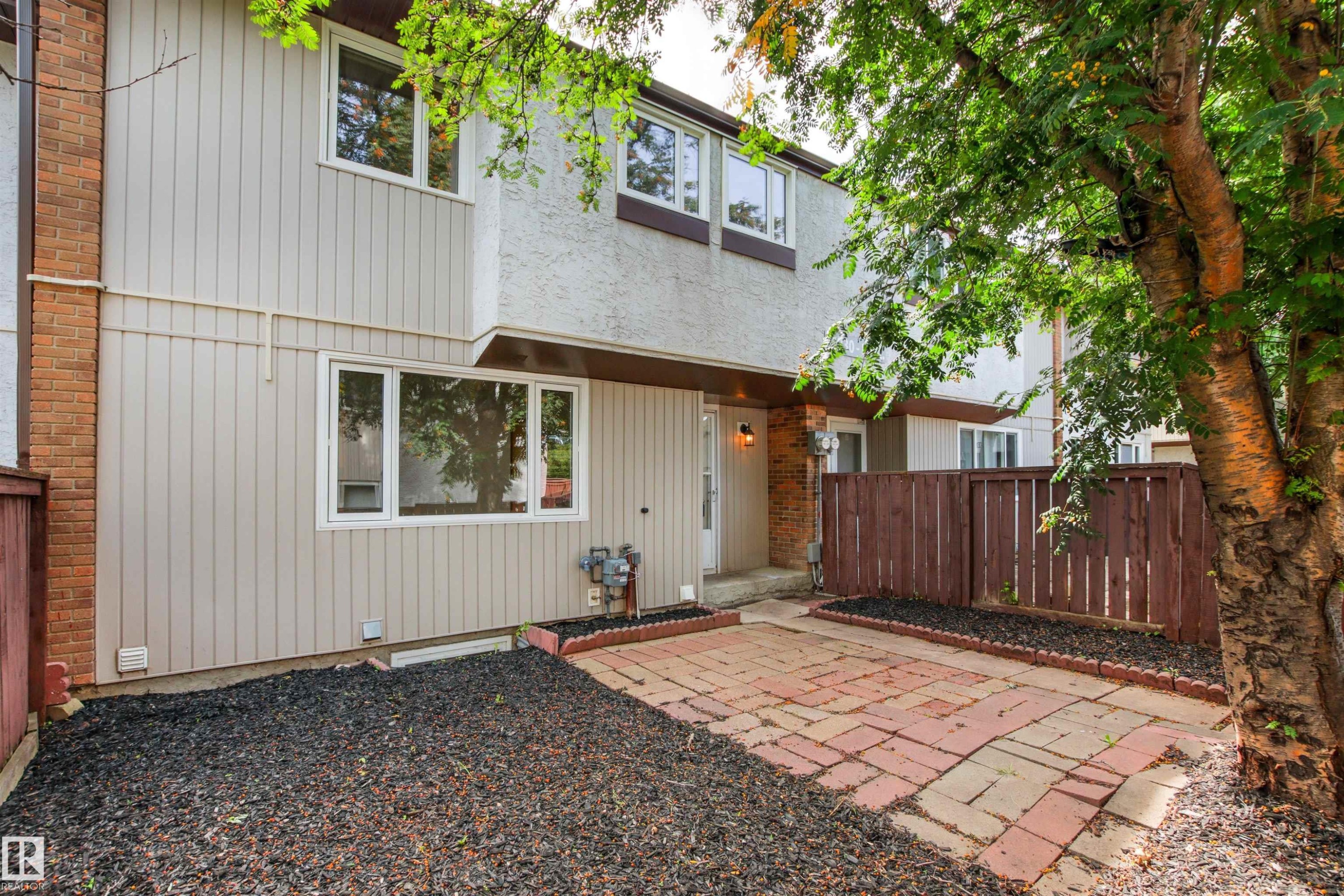Modern townhome exterior featuring a welcoming entrance with wood-grain cladding siding, multi-pane windows, and brick detailing - #9 14230 80 St Nw, Edmonton, AB - Outdoor With Exterior