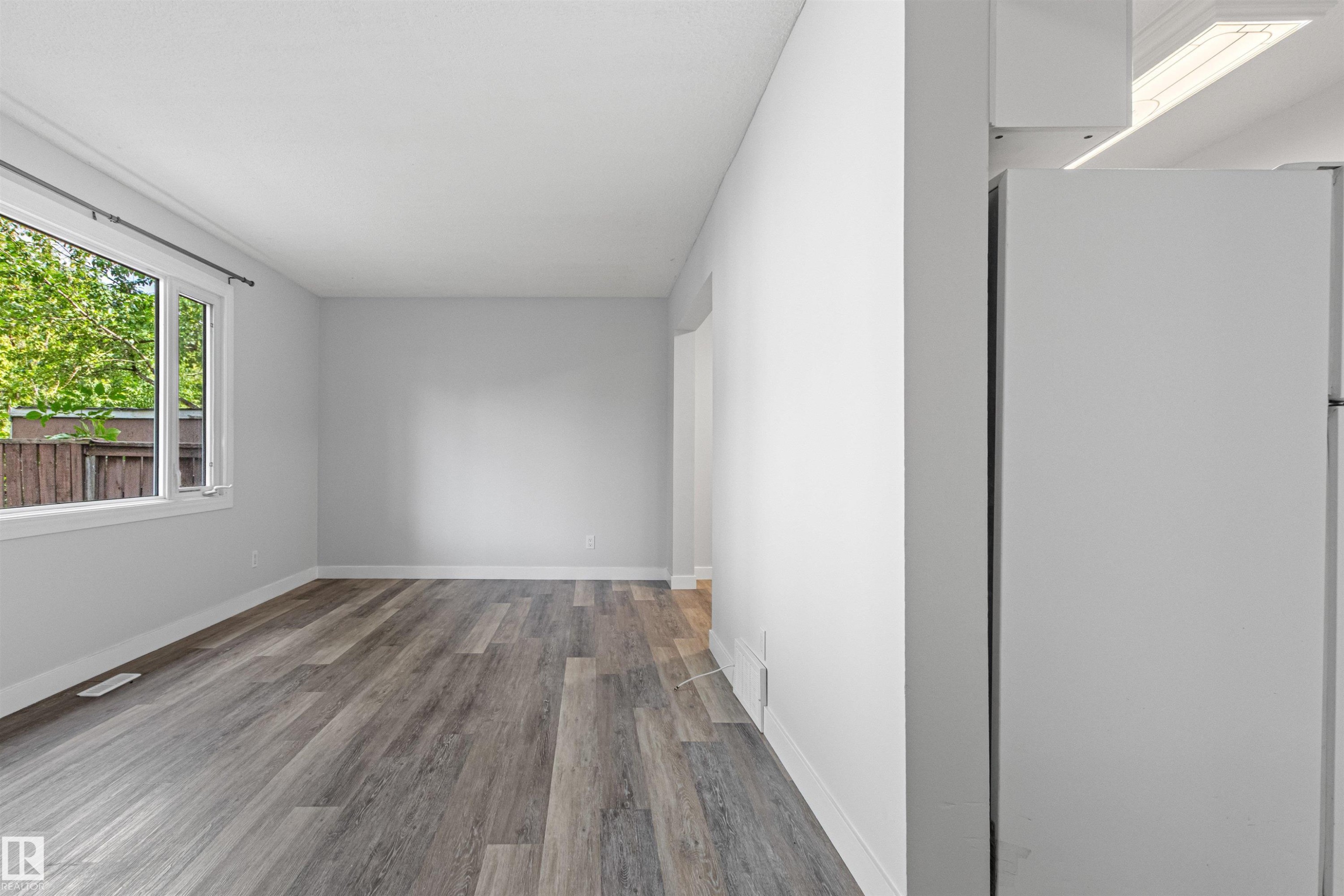 Bright, light-filled room featuring pristine white walls, recessed ceiling lighting, and engineered wood-finish flooring in a warm gray tone - #9 14230 80 St Nw, Edmonton, AB - Indoor Photo Showing Other Room