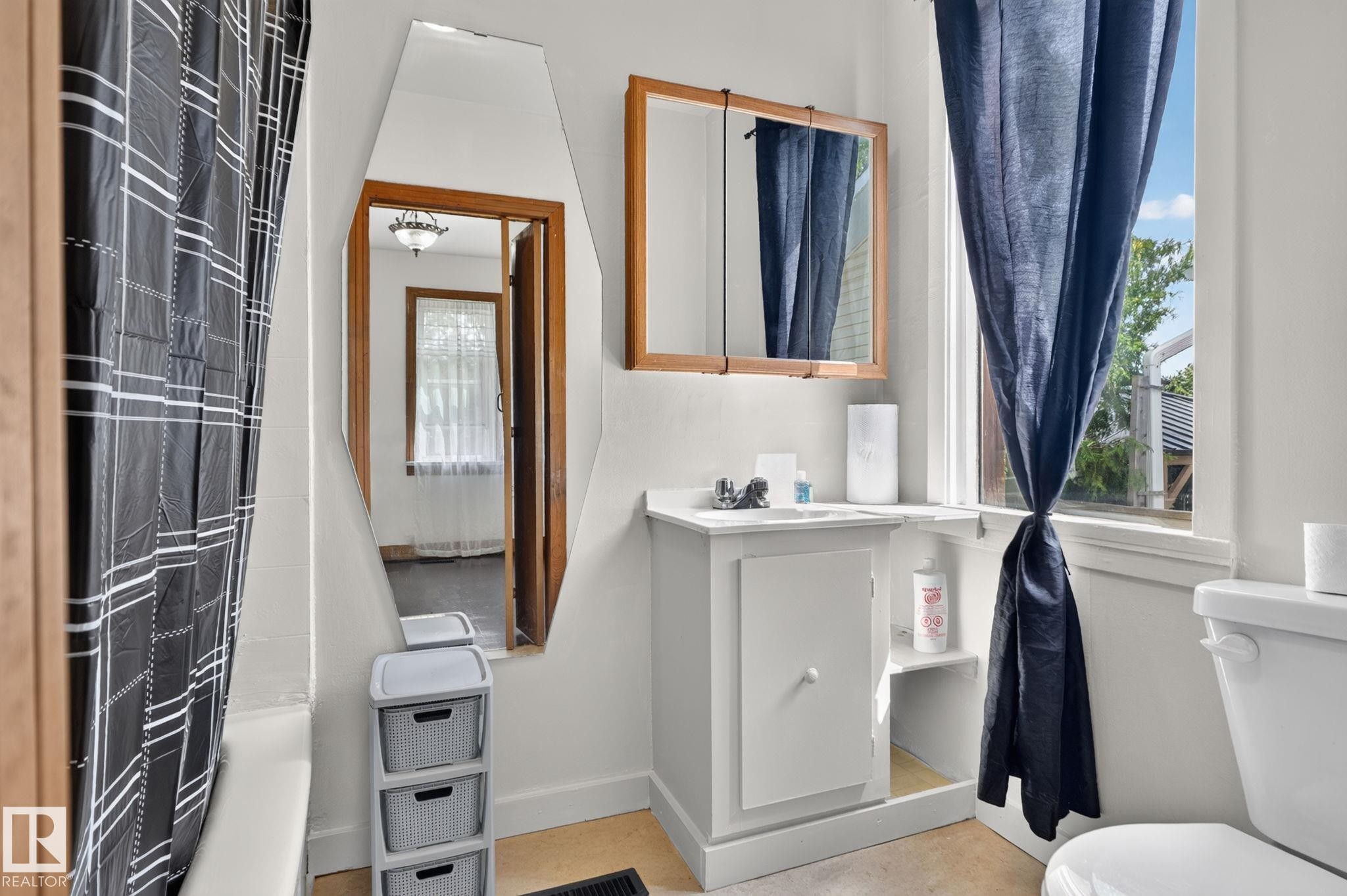 Bright, light-filled bathroom featuring a pedestal sink with chrome faucet, wood-frame mirror, wood-finish flooring, and white subway tile walls - 9921 109 Street, Fort Saskatchewan, AB - Indoor