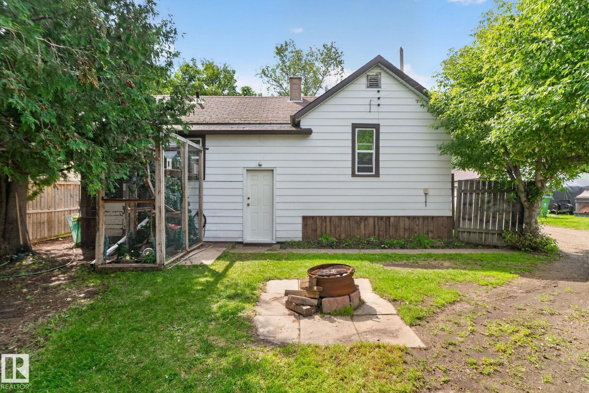 White siding exterior with a dark trim window, a side entry door, and a built-in outdoor enclosure - 9921 109 Street, Fort Saskatchewan, AB - Outdoor