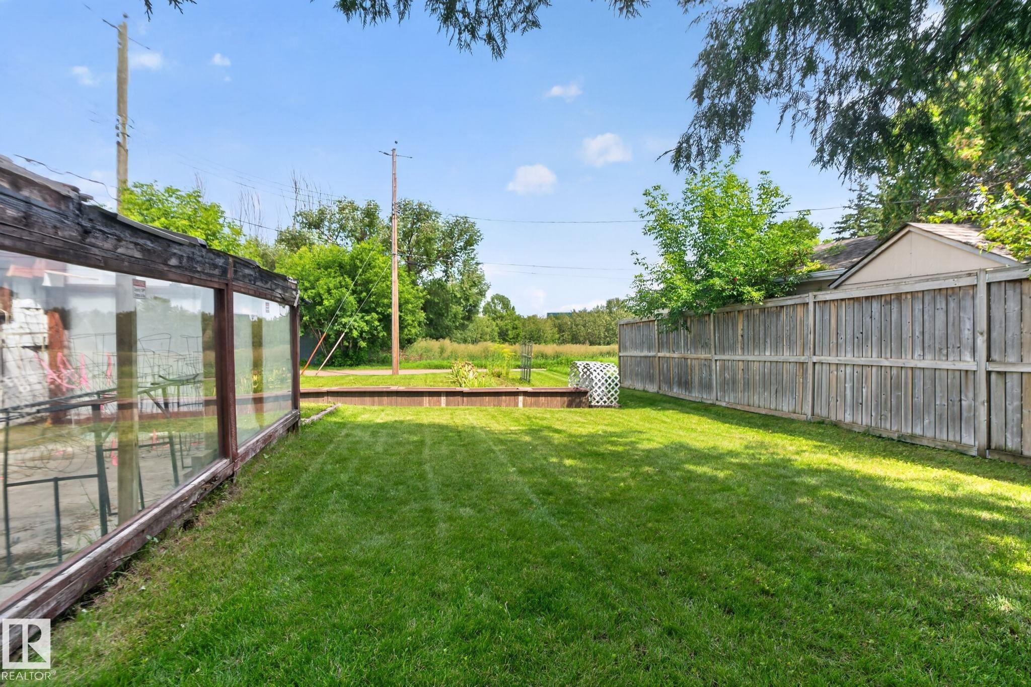 Expansive lawn area with a wood privacy fence and a glass-enclosed structure - 9921 109 Street, Fort Saskatchewan, AB - Outdoor