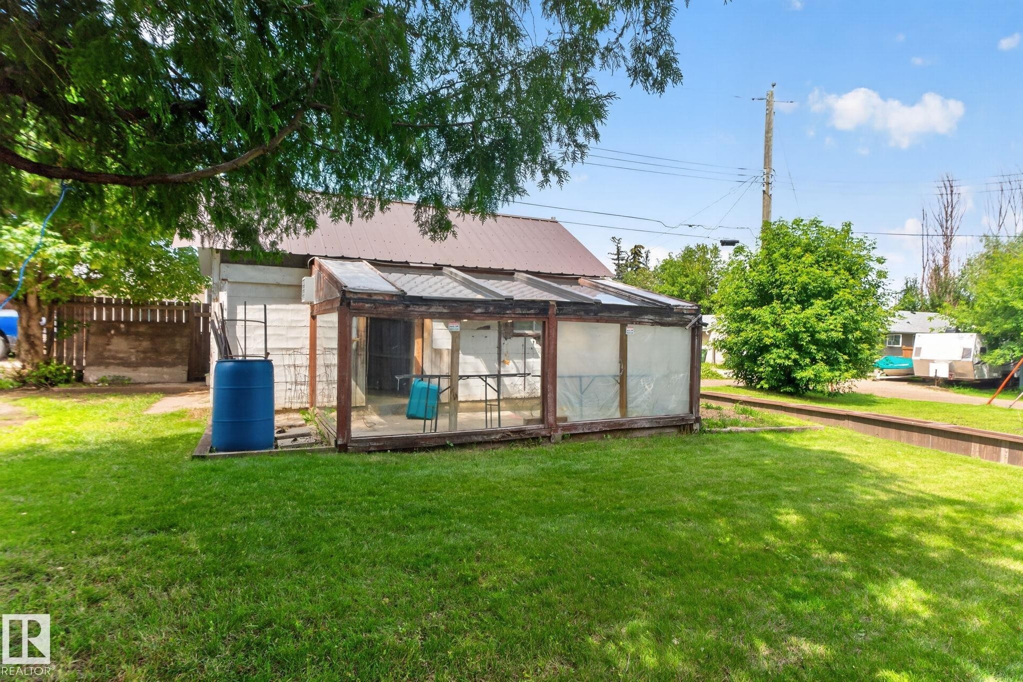 Grassy yard space featuring a greenhouse structure with a translucent roof and wood framing, and a partial privacy fence - 9921 109 Street, Fort Saskatchewan, AB - Outdoor