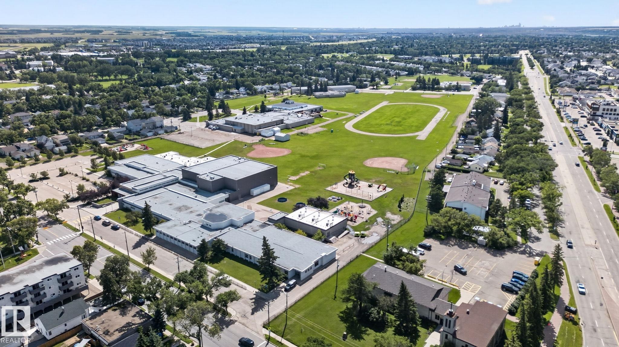 Aerial view showcasing expansive grounds with a large rectangular athletic field, multiple modern institutional buildings with clean architectural lines, mature landscaping throughout the property, and a manicured lawn with established trees - 9921 109 Street, Fort Saskatchewan, AB - Outdoor With View