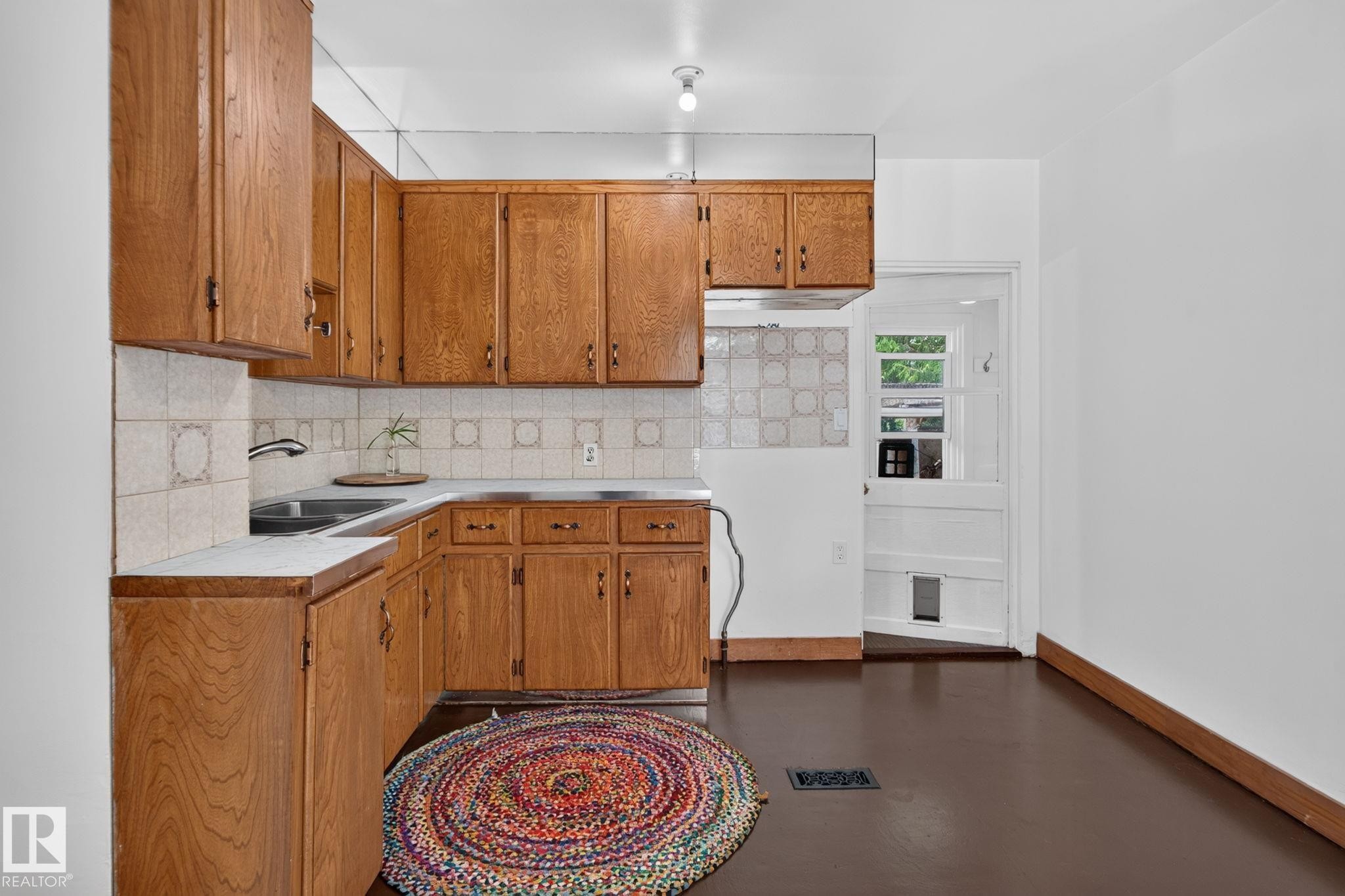 Wood-finish cabinetry, tile backsplash, laminate countertops, and a stainless steel sink - 9921 109 Street, Fort Saskatchewan, AB - Indoor Photo Showing Kitchen With Double Sink