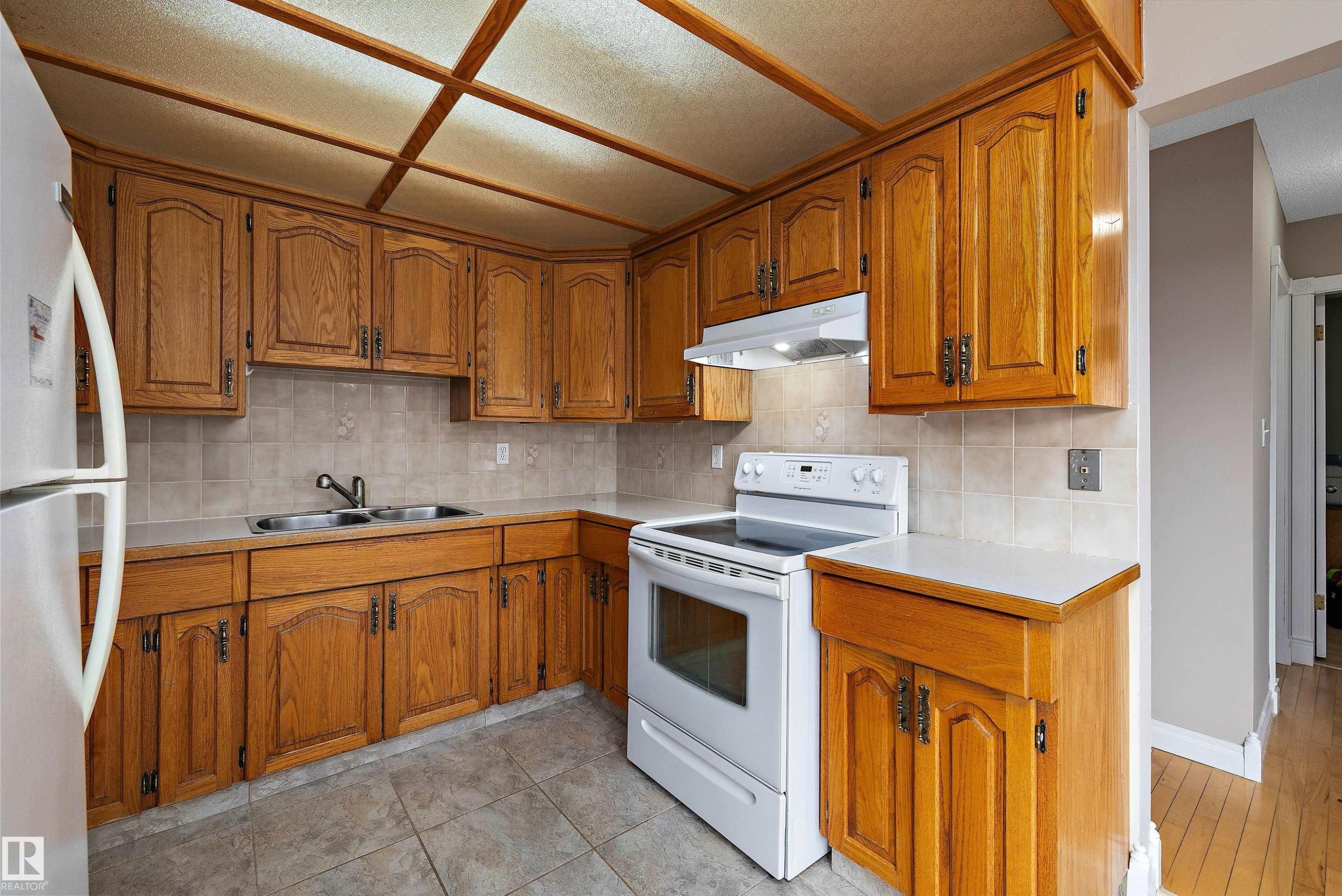 Wood-finish cabinetry with dark hardware, solid surface countertops, a tile backsplash, and a drop ceiling with integrated lighting - 3511 73 Street Nw, Edmonton, AB - Indoor Photo Showing Kitchen With Double Sink