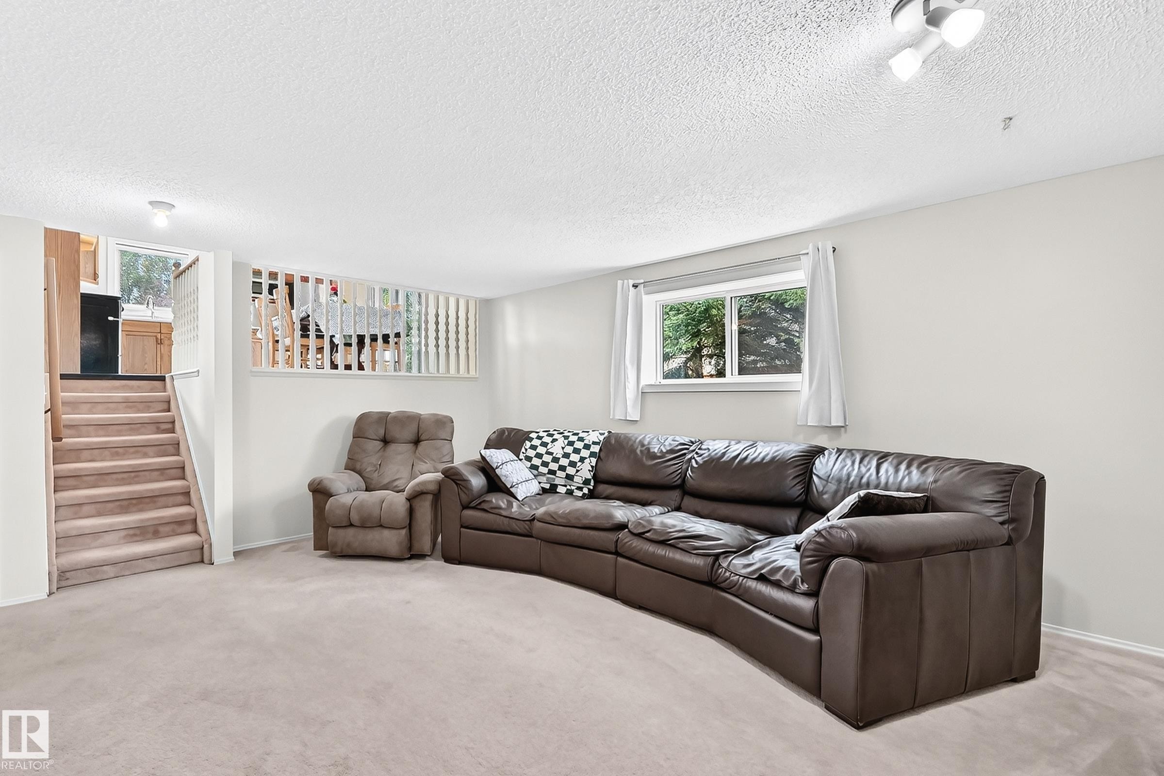 Carpeted flooring extending to the staircase, white painted walls, natural light from a double window, and a built-in privacy screen - 2404 37 Street Nw, Edmonton, AB - Indoor Photo Showing Living Room