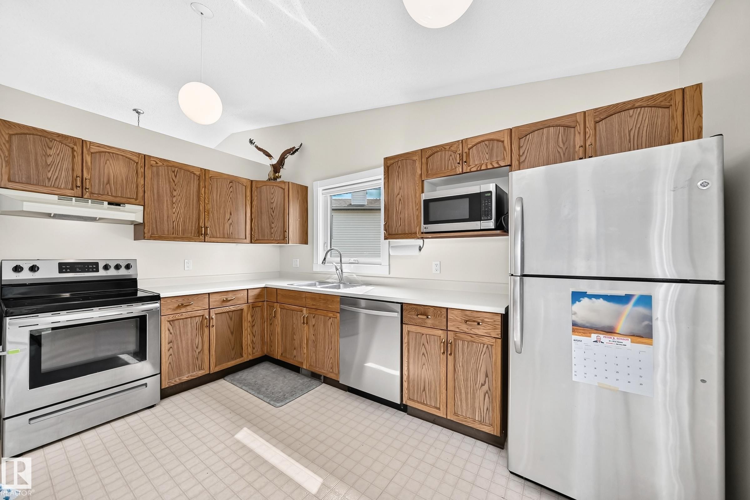 Kitchen featuring wood-finish cabinetry, stainless steel appliances, and a double basin sink - 2404 37 Street Nw, Edmonton, AB - Indoor Photo Showing Kitchen With Double Sink