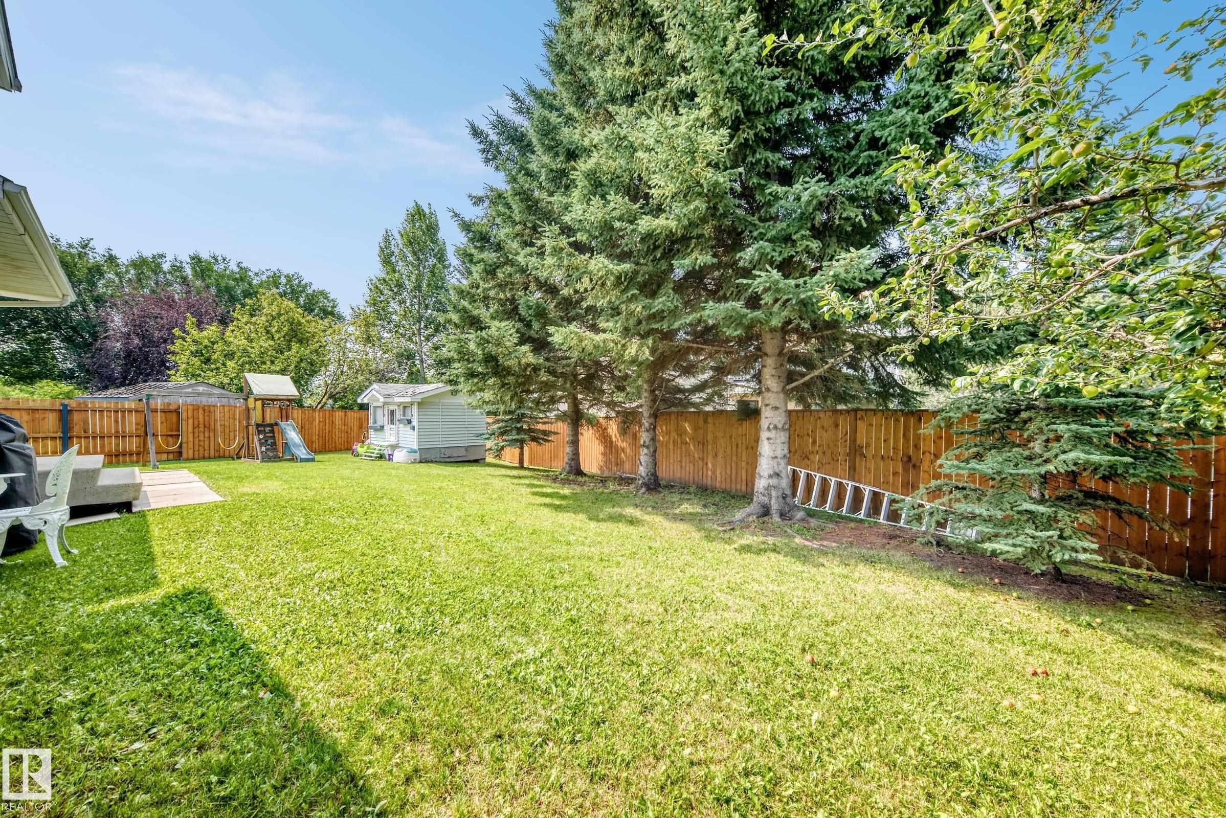 Expansive backyard featuring a large lawn, mature trees, and a wood privacy fence - 2404 37 Street Nw, Edmonton, AB - Outdoor With Backyard