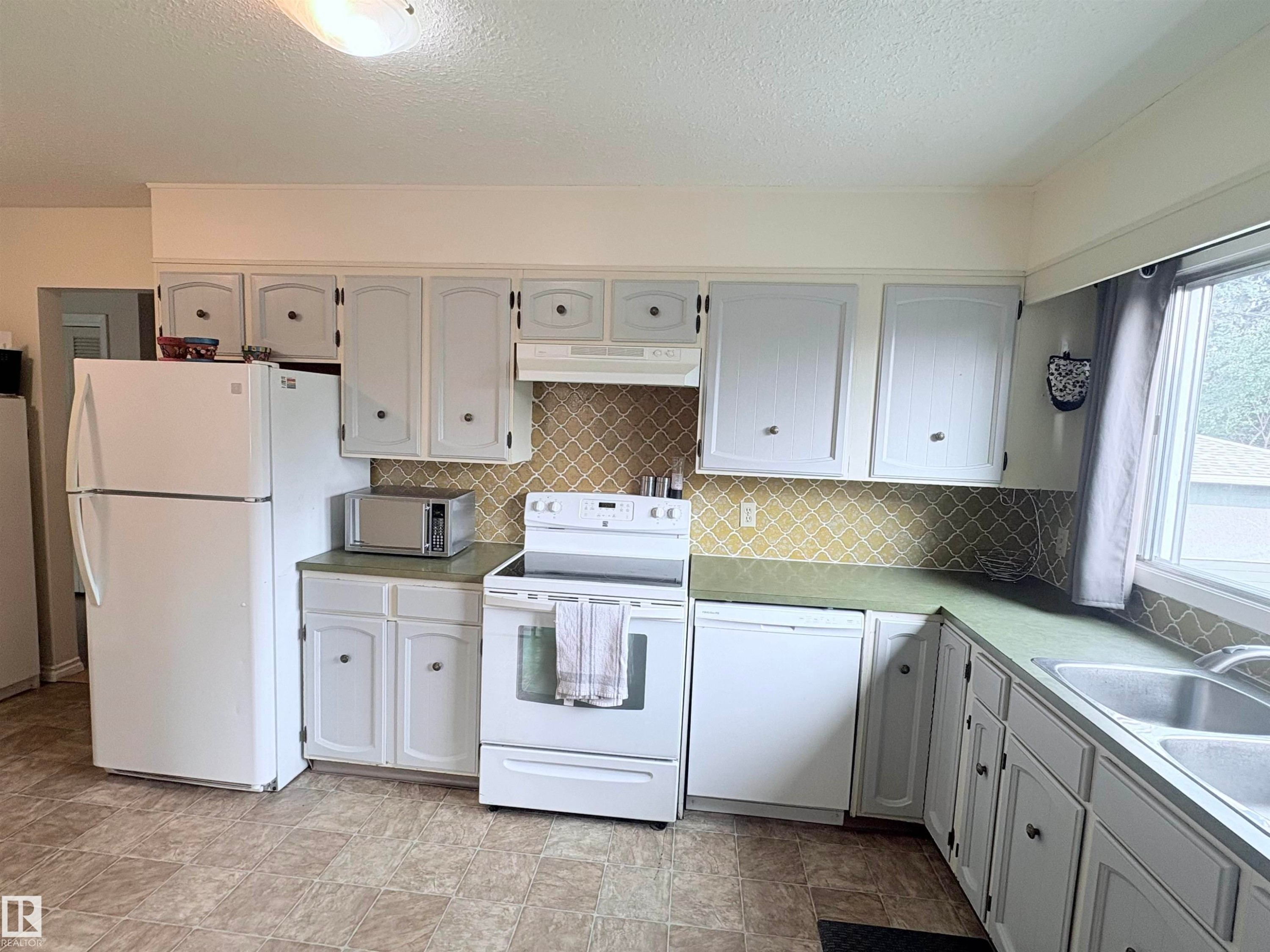 Kitchen featuring white cabinetry, green countertops, and a patterned backsplash - 5411 44 Ave, Wetaskiwin, AB - Indoor Photo Showing Kitchen