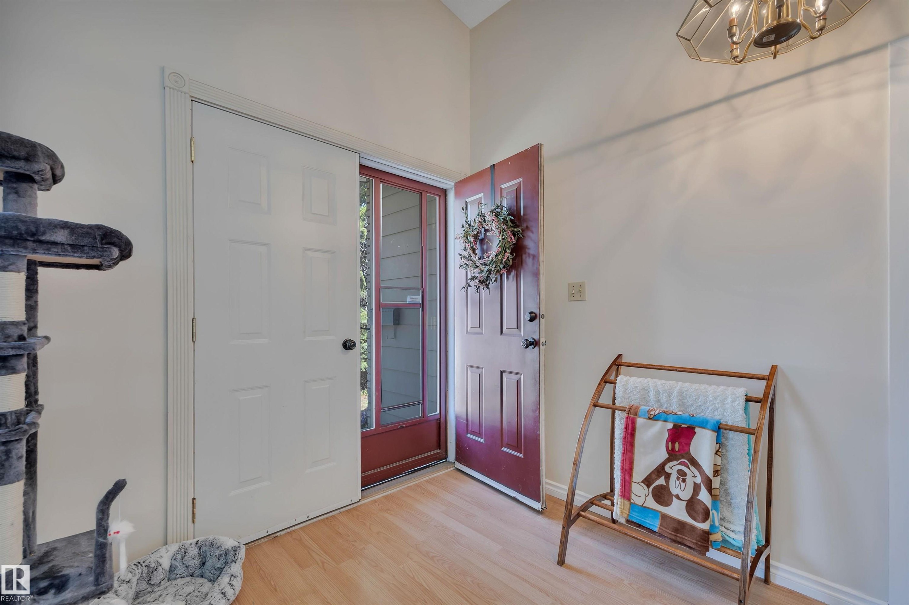 Entryway featuring light wood-finish flooring, a red front door with a glass screen door, and a white six-panel interior door - 5411 44 Ave, Wetaskiwin, AB - Indoor Photo Showing Other Room