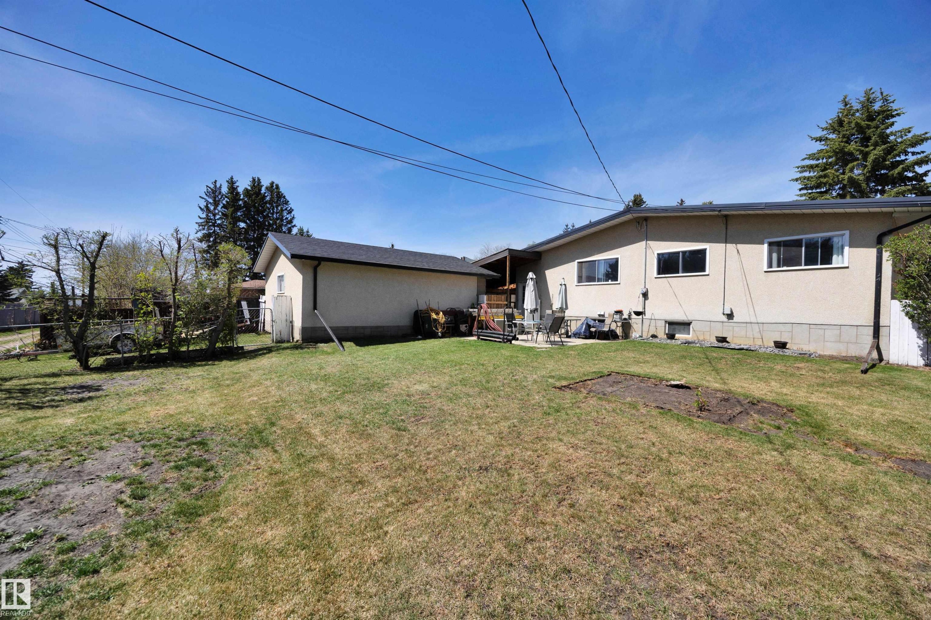 Expansive rear yard featuring a detached auxiliary building, concrete patio, and mature perimeter trees - 5411 44 Ave, Wetaskiwin, AB - Outdoor