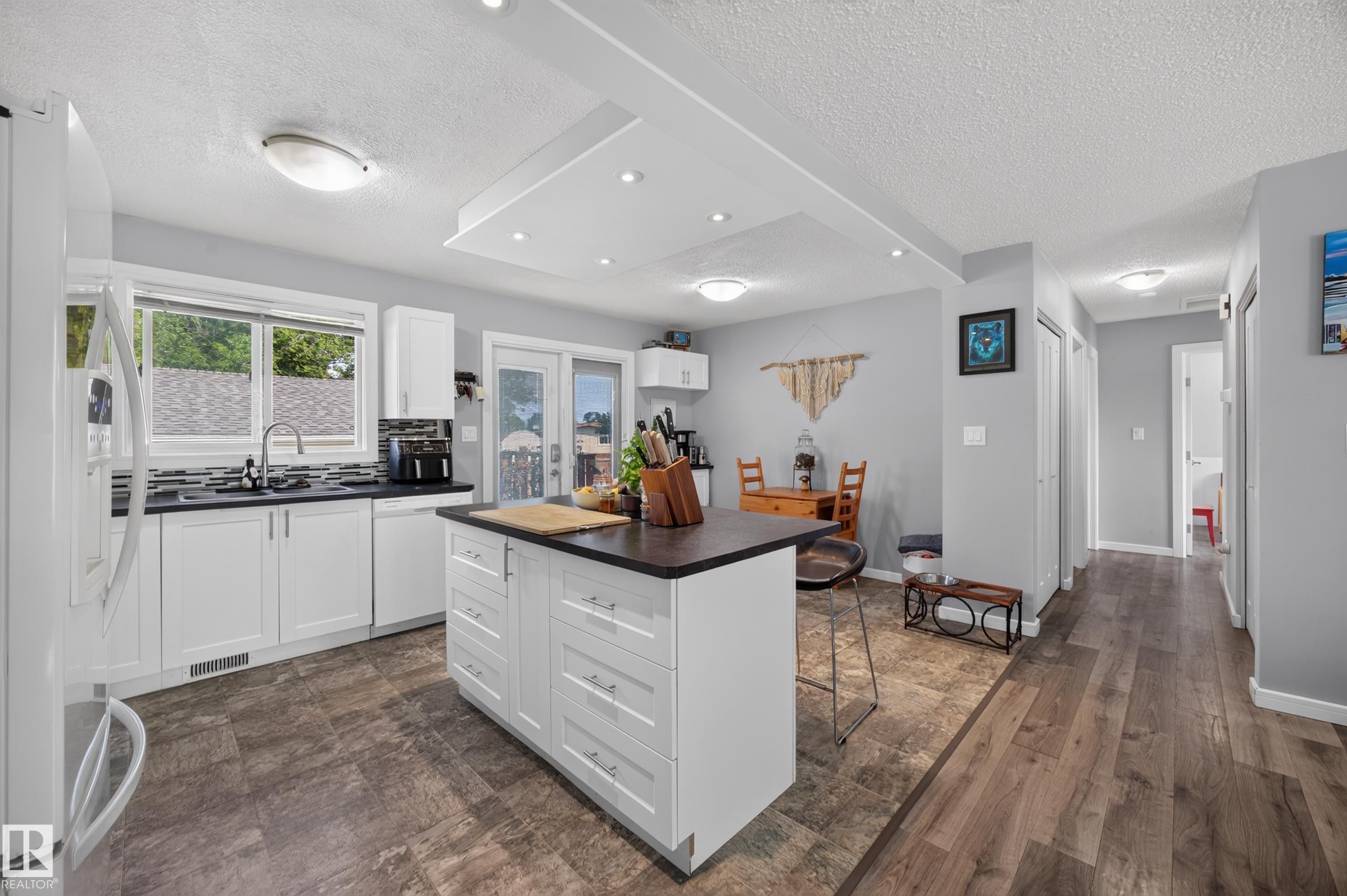 Modern kitchen featuring white cabinetry with a large center island, wood-finish flooring throughout, stainless steel appliances, and abundant natural light from multi-pane windows - 156 Clareview Road Nw, Edmonton, AB - Indoor Photo Showing Kitchen