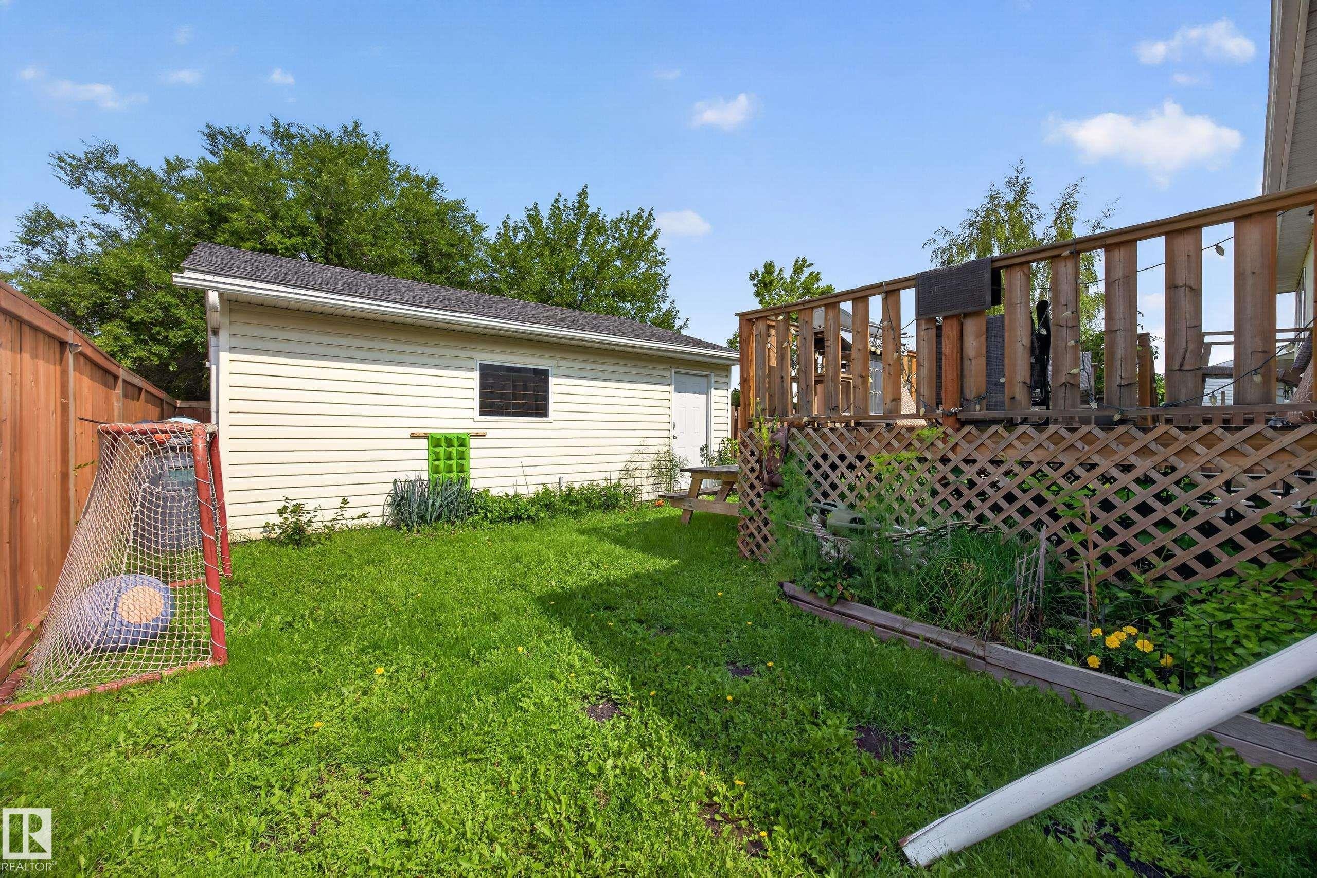 Rear yard featuring a wooden privacy fence, a detached auxiliary building with siding, a wooden deck with lattice skirting, and a manicured lawn area - 156 Clareview Road Nw, Edmonton, AB - Outdoor