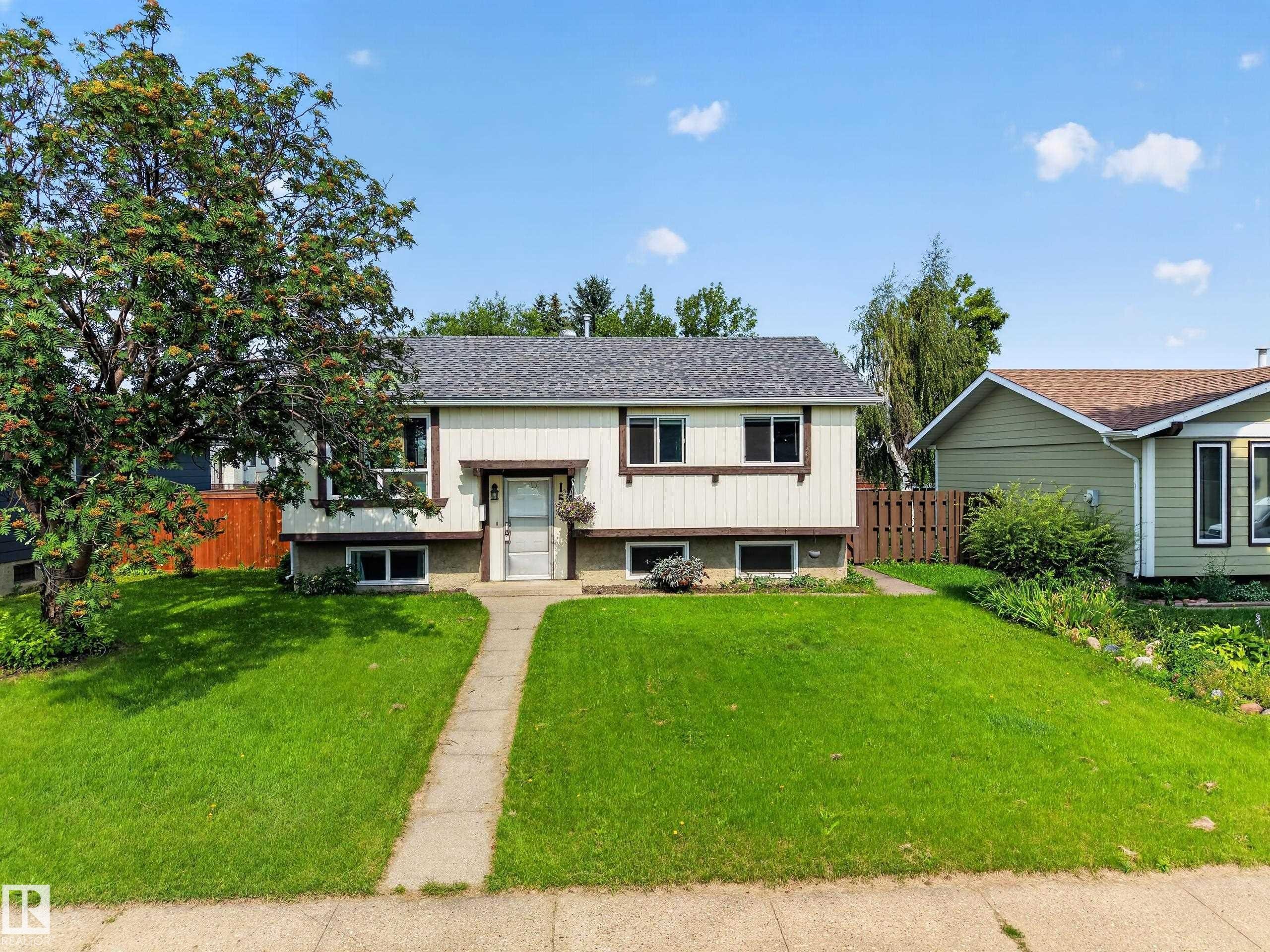 Welcoming split-level home featuring a clean cream and charcoal exterior with updated roofing, positioned on a spacious manicured lawn anchored by mature trees - 156 Clareview Road Nw, Edmonton, AB - Outdoor