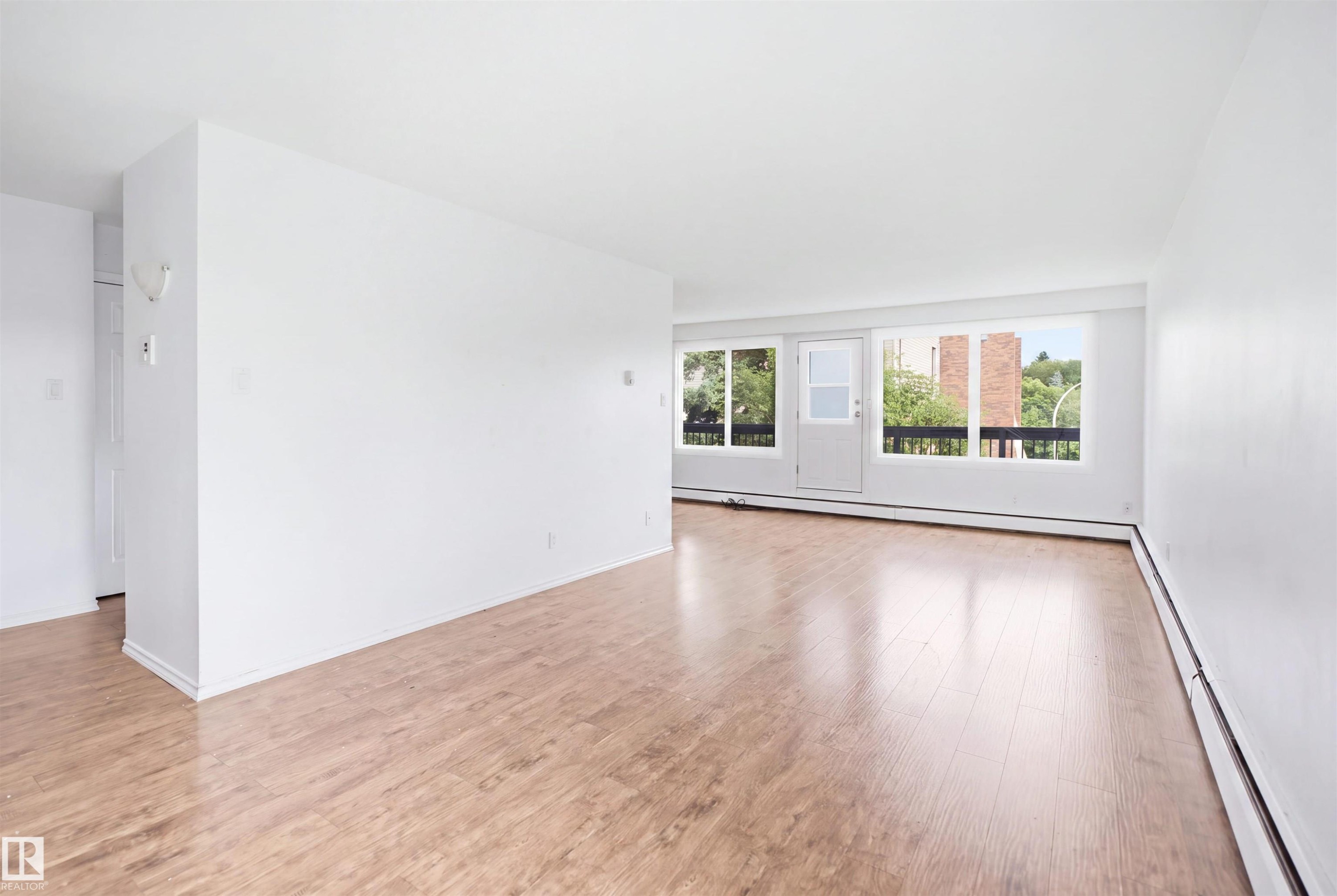 Expansive room featuring wood-finish flooring, white walls, and a large window providing ample natural illumination - 7825 159 Street Nw, Edmonton, AB - Indoor