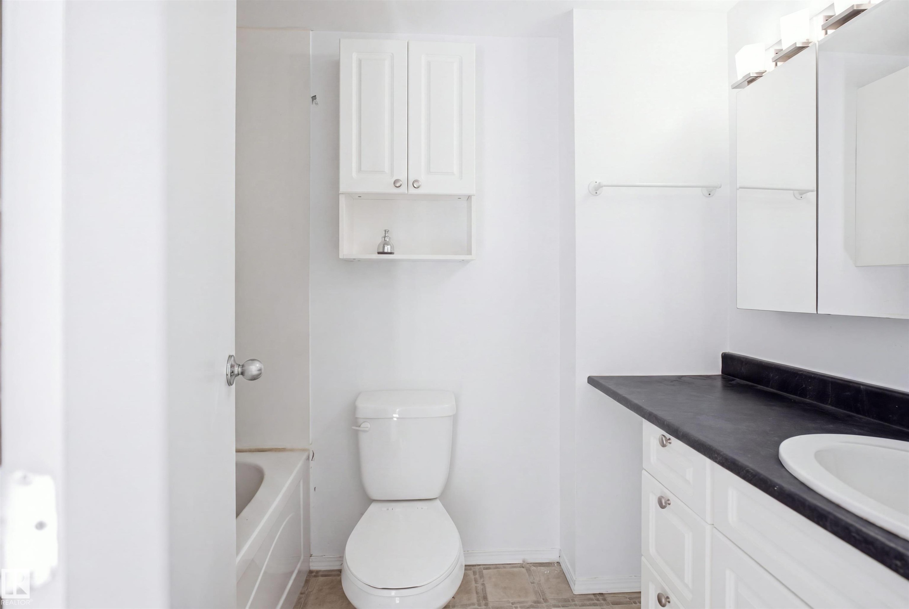 White vanity with black countertop and integrated sink, white wall-mounted medicine cabinet, toilet, and white wall-mounted storage cabinet - 7825 159 Street Nw, Edmonton, AB - Indoor Photo Showing Bathroom