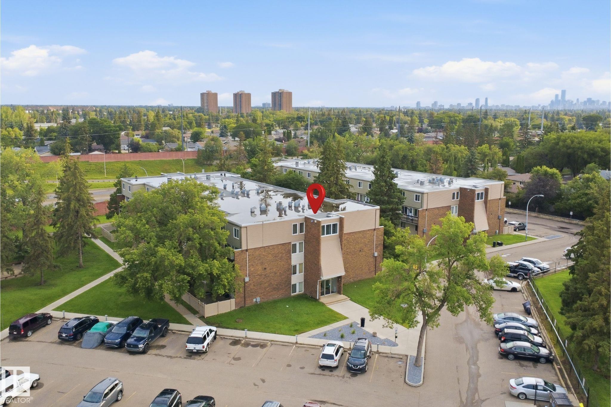 Modern brick-constructed residential building featuring a flat roofline, expansive rooftop terrace with multiple seating areas, and ample surface parking - 7825 159 Street Nw, Edmonton, AB - Outdoor With View