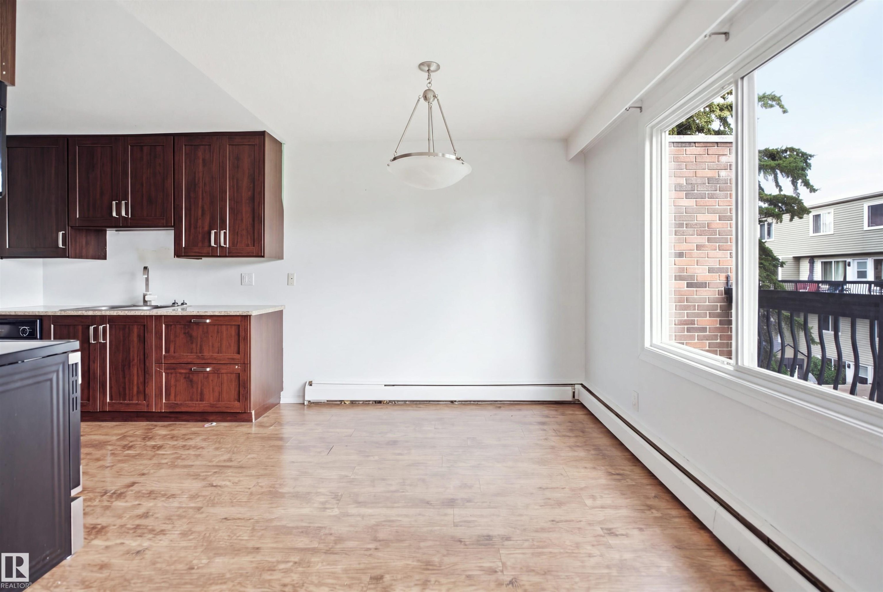 Wood-finish flooring, dark wood cabinetry, light-toned countertop, a stainless steel sink, and a large window - 7825 159 Street Nw, Edmonton, AB - Indoor Photo Showing Kitchen