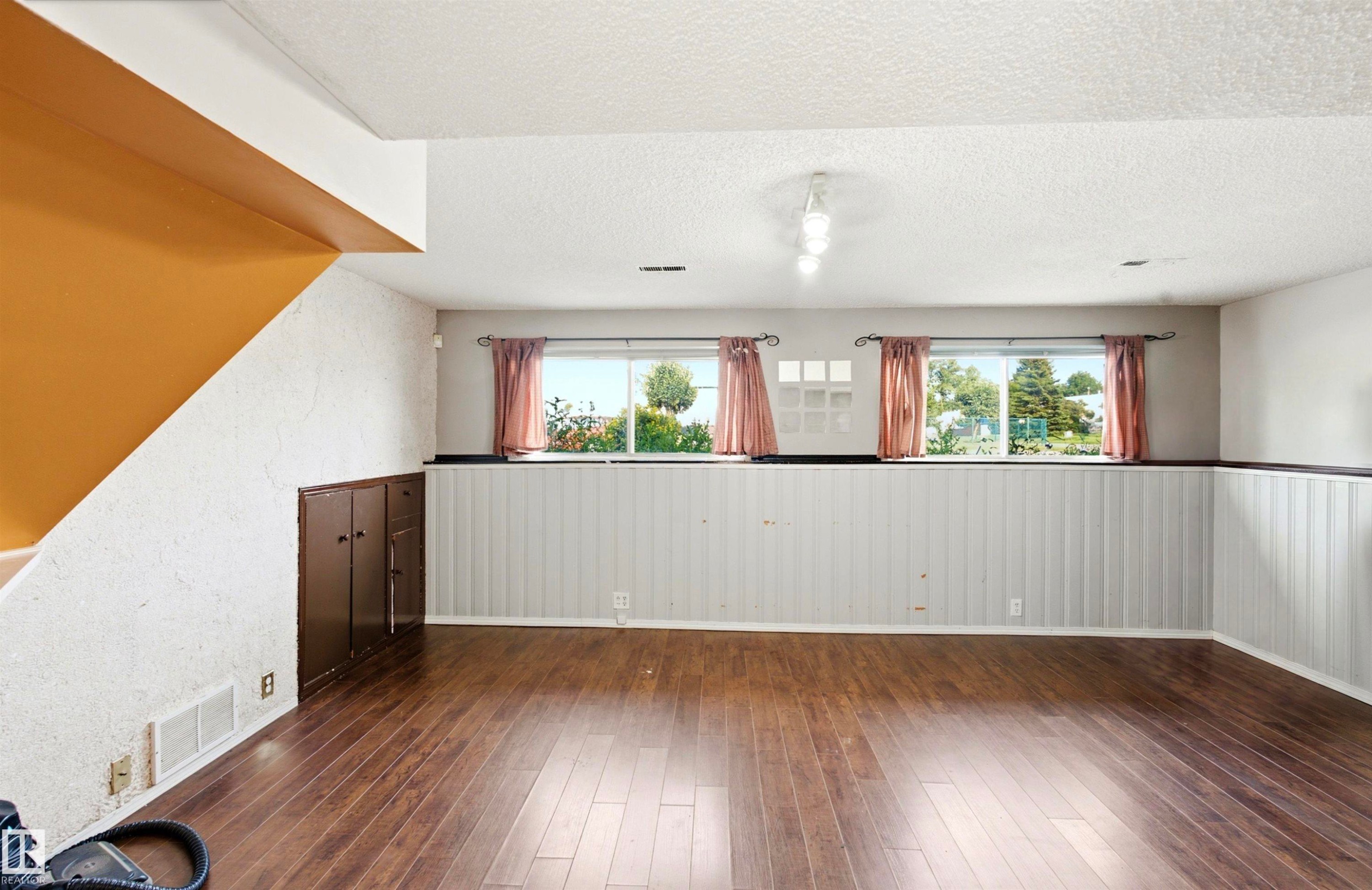 Wood-finish flooring throughout, featuring a white textured wall finish, and white paneled wainscoting - 13604 90A Street Nw, Edmonton, AB - Indoor Photo Showing Other Room