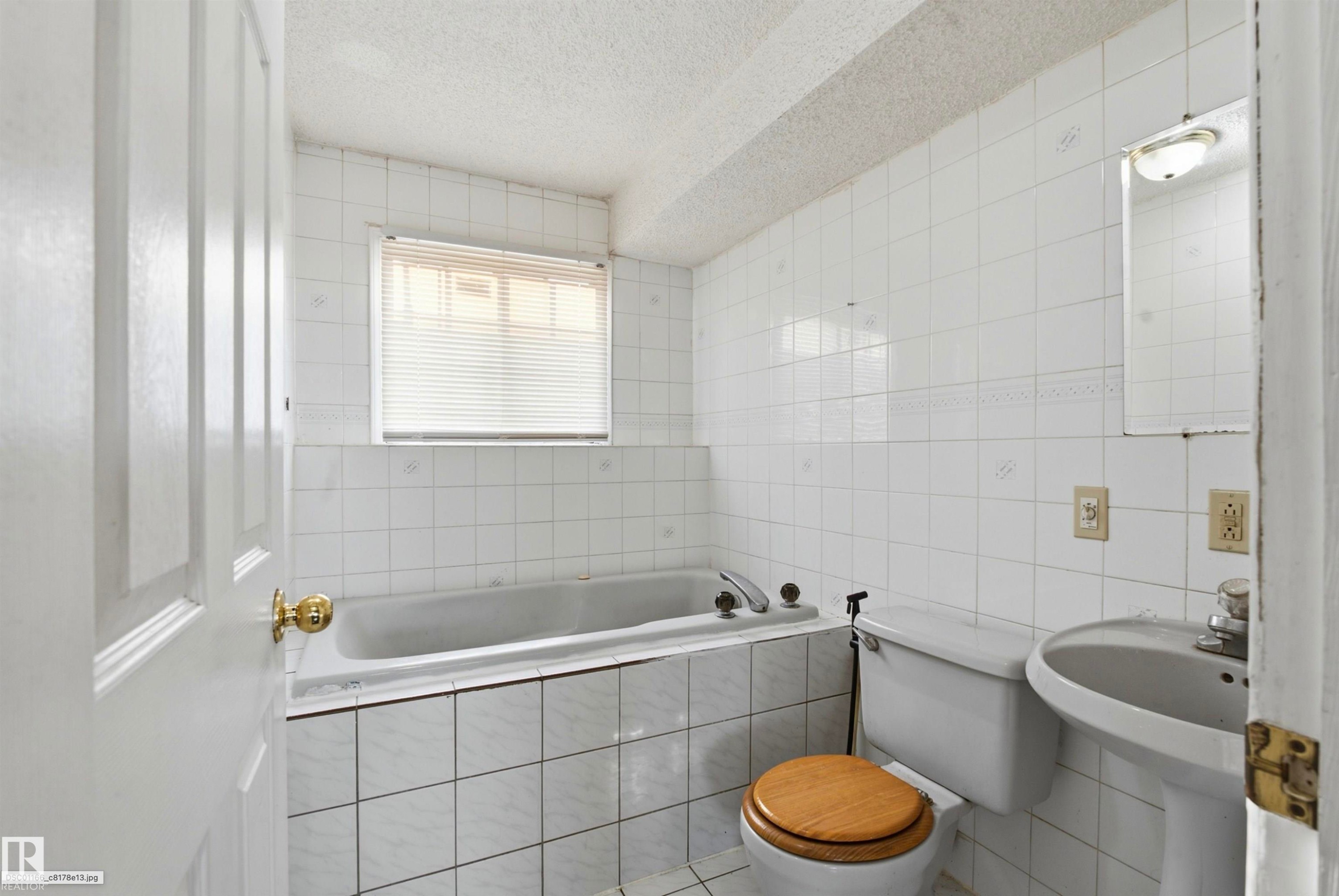 White ceramic tile walls with a decorative border, pedestal sink, and built-in bathtub with tile surround - 13604 90A Street Nw, Edmonton, AB - Indoor Photo Showing Bathroom