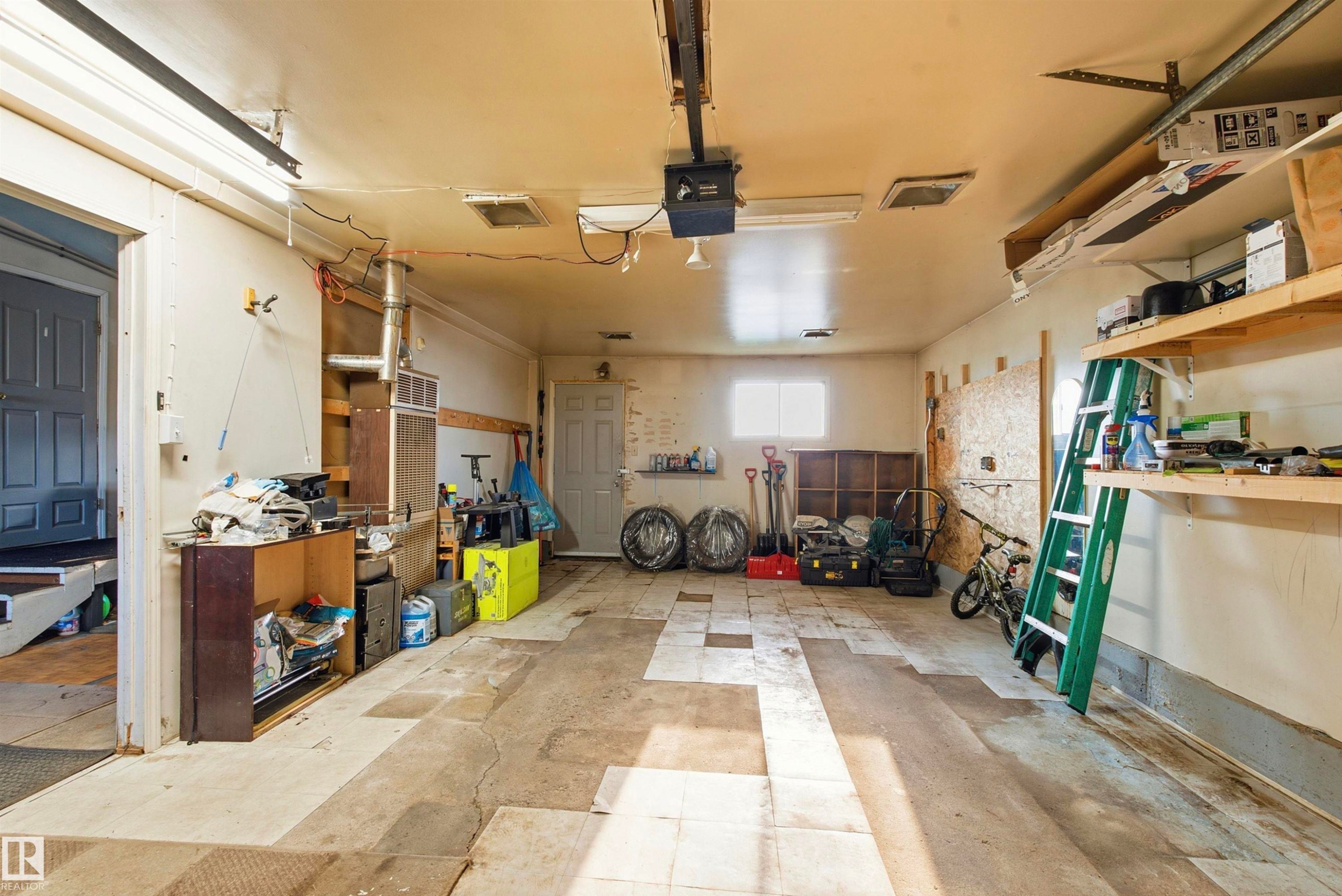 Garage space featuring an overhead garage door opener, overhead lighting, and built-in shelving - 13604 90A Street Nw, Edmonton, AB - Indoor Photo Showing Garage