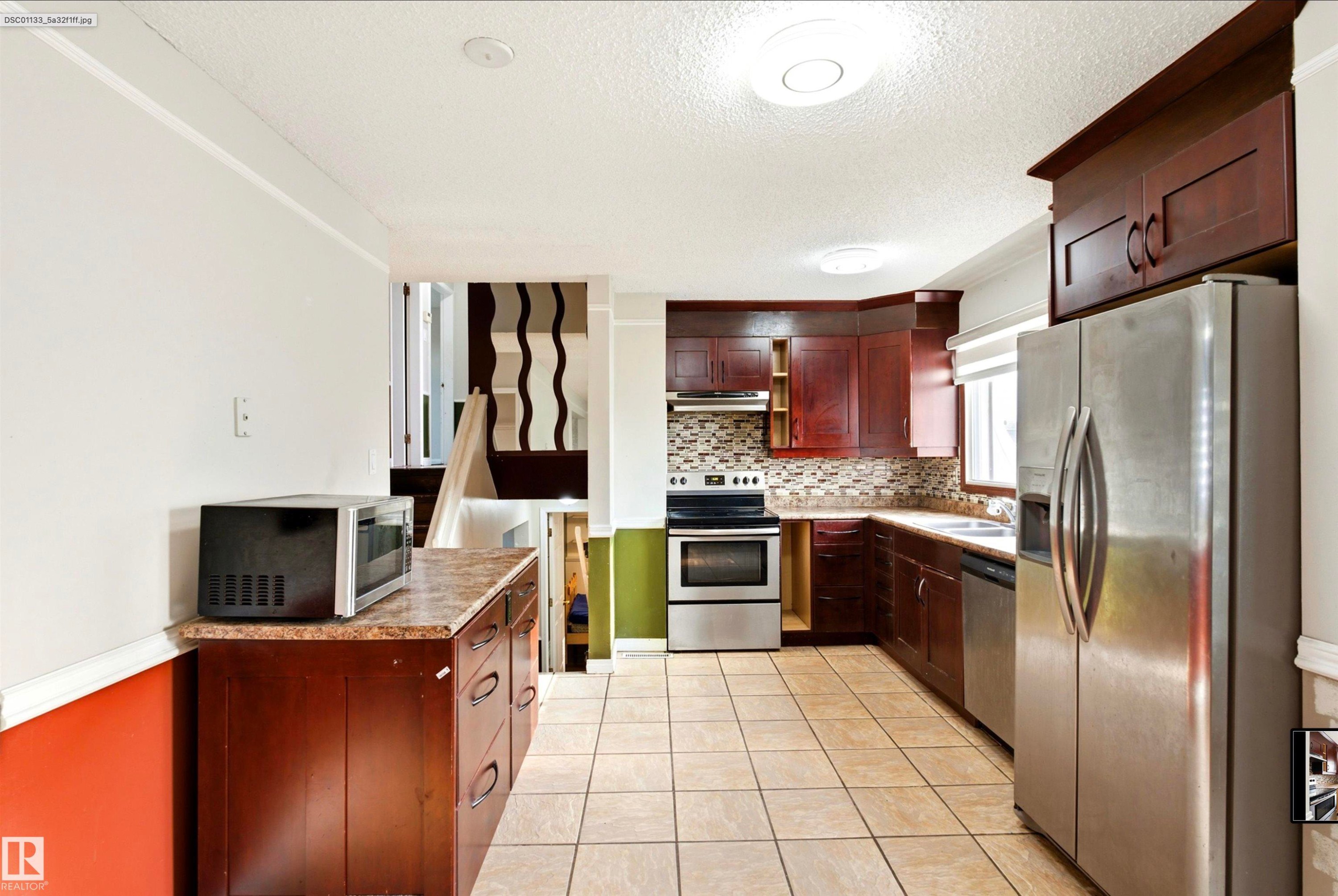 Galley kitchen featuring ceramic tile flooring, dark wood-finish cabinetry, stainless steel appliances, and a tiled backsplash - 13604 90A Street Nw, Edmonton, AB - Indoor Photo Showing Kitchen With Stainless Steel Kitchen With Double Sink