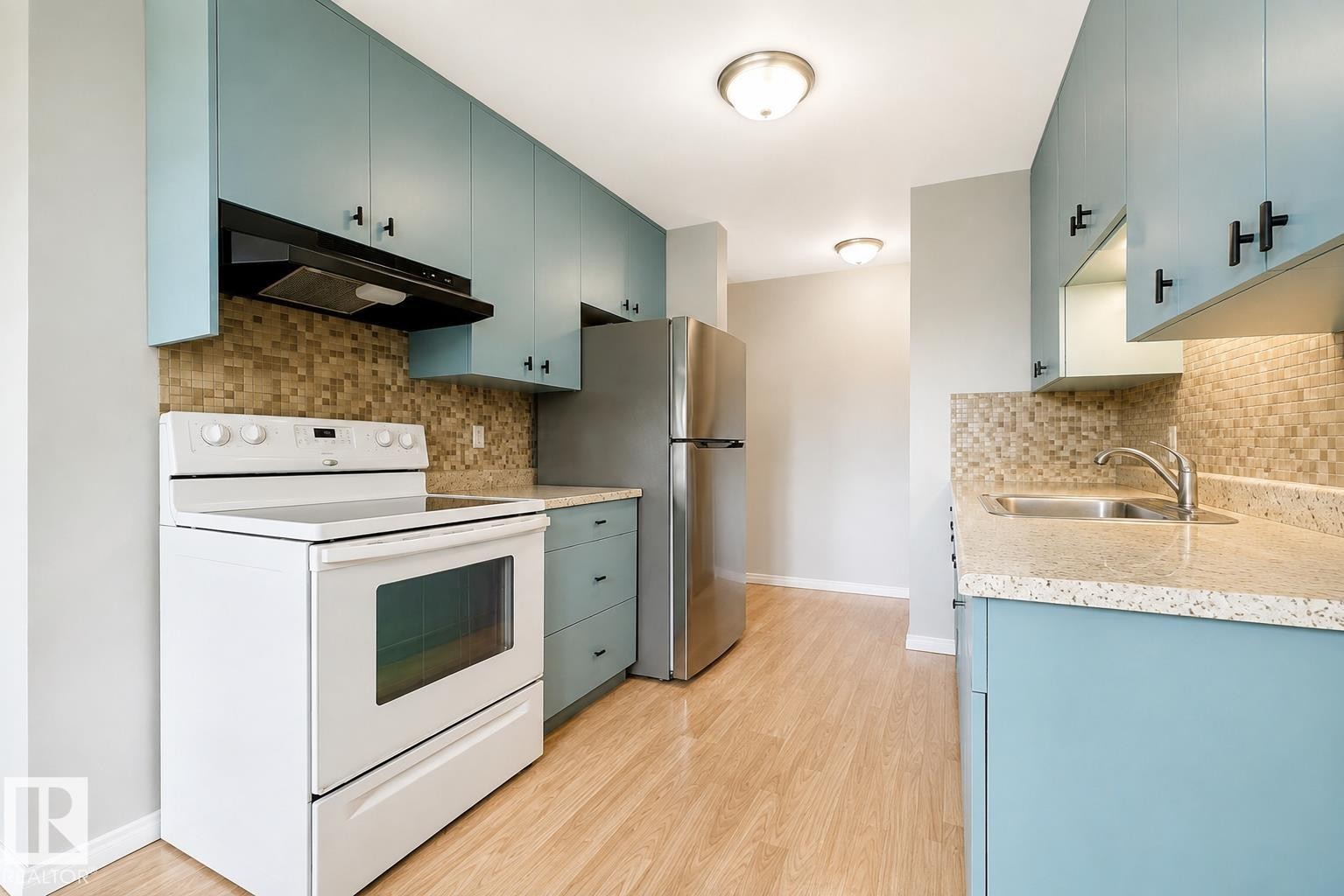 Full kitchen featuring light blue cabinetry, mosaic tile backsplash, wood-finish flooring, a stainless steel refrigerator, and a white electric range - #31 11255 31 Av Nw, Edmonton, AB - Indoor Photo Showing Kitchen