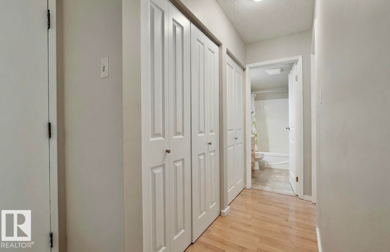 Hallway with wood-finish flooring, two sets of white bifold doors, and recessed ceiling lighting - #31 11255 31 Av Nw, Edmonton, AB - Indoor Photo Showing Other Room