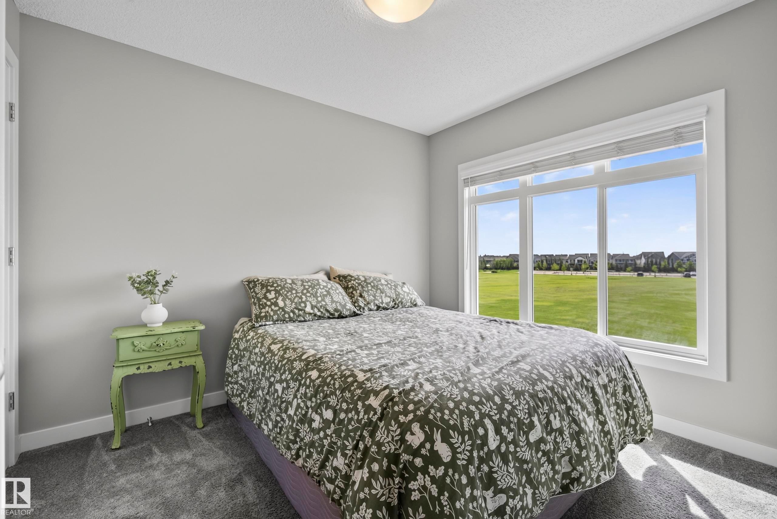Wall-to-wall carpeting and neutral wall tones complement the large window with white trim, allowing natural light to illuminate the space - 45 Joyal Way, St. Albert, AB - Indoor Photo Showing Bedroom