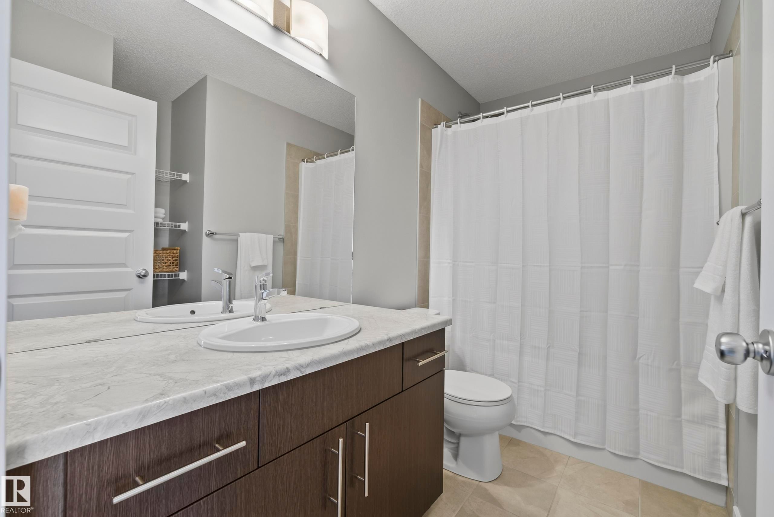 Spacious bathroom featuring a dual vanity with a light-toned countertop, wood-finish cabinetry, and a full-width mirror - 45 Joyal Way, St. Albert, AB - Indoor Photo Showing Bathroom
