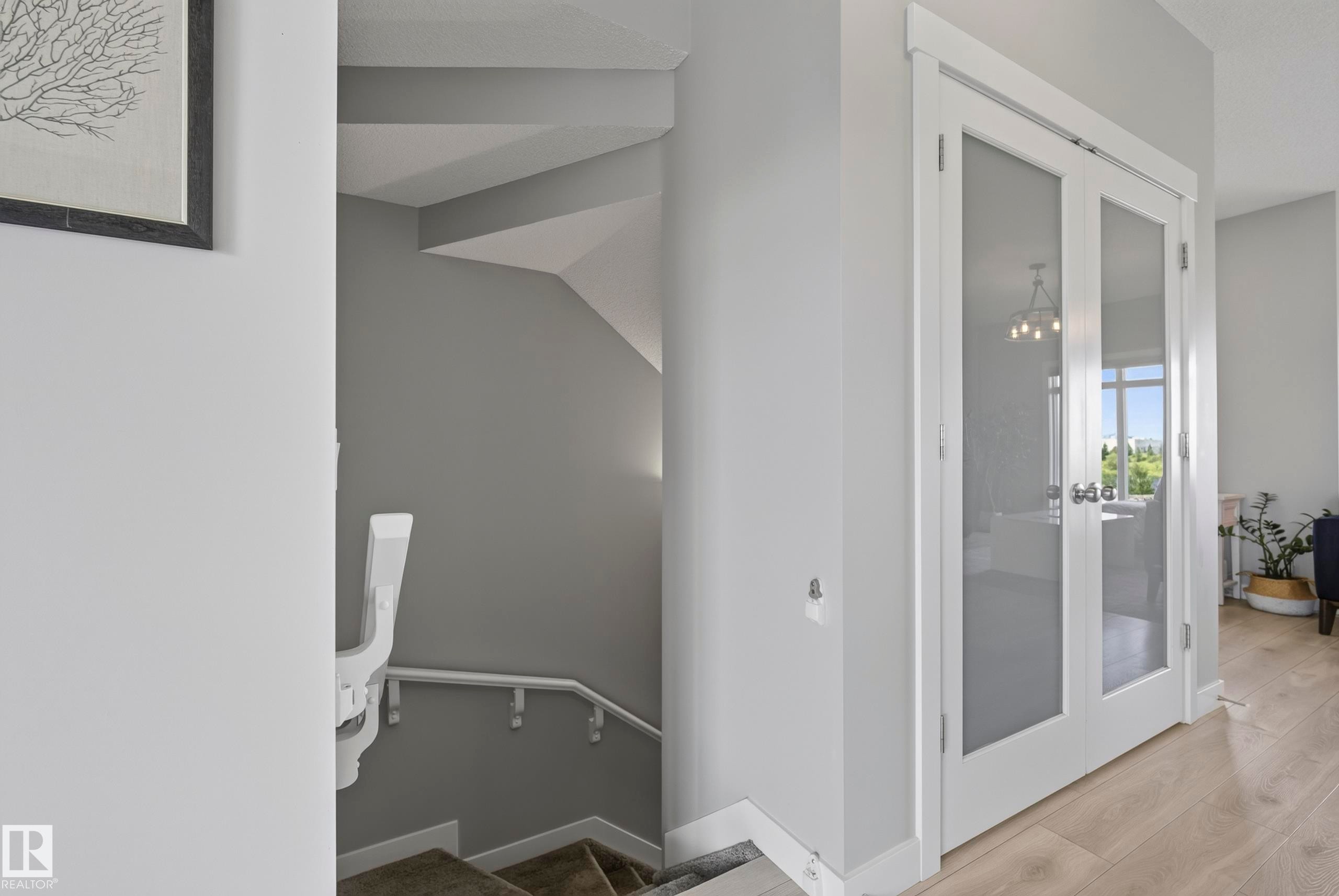 White interior doors with frosted glass panels, wood-finish flooring, and a carpeted staircase with a white handrail - 45 Joyal Way, St. Albert, AB - Indoor Photo Showing Other Room