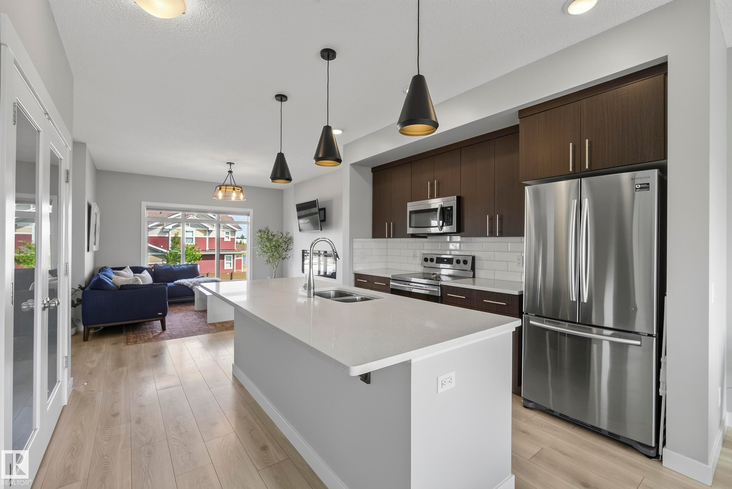 Open-concept living area with wood-finish flooring, a kitchen island with a sink, and stainless steel appliances - 45 Joyal Way, St. Albert, AB - Indoor Photo Showing Kitchen With Double Sink With Upgraded Kitchen