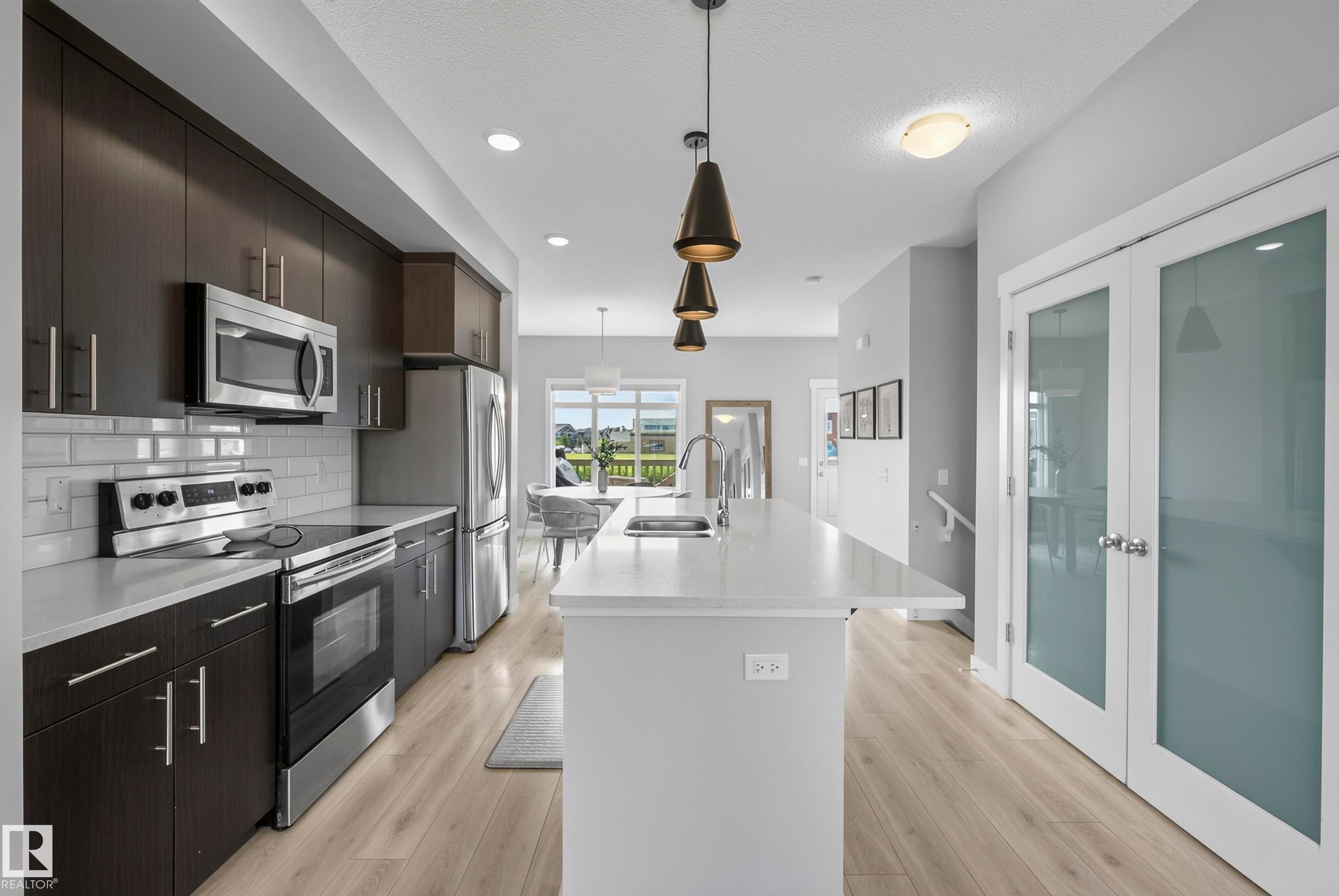 Modern kitchen featuring stainless steel appliances, dark wood-finish cabinetry, light countertops, and a subway tile backsplash - 45 Joyal Way, St. Albert, AB - Indoor Photo Showing Kitchen With Upgraded Kitchen