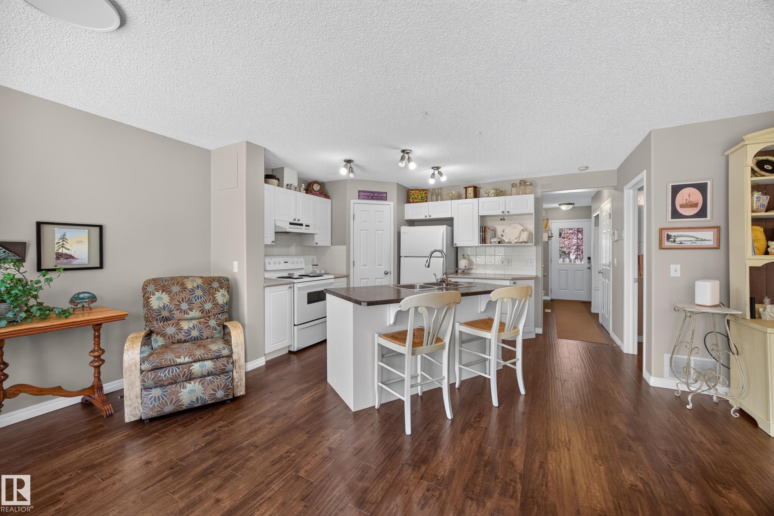 Kitchen and living area featuring wood-finish flooring, light gray wall paint, white cabinetry, a kitchen island with seating, and white appliances - #7 155 Crocus Cr, Sherwood Park, AB - Indoor