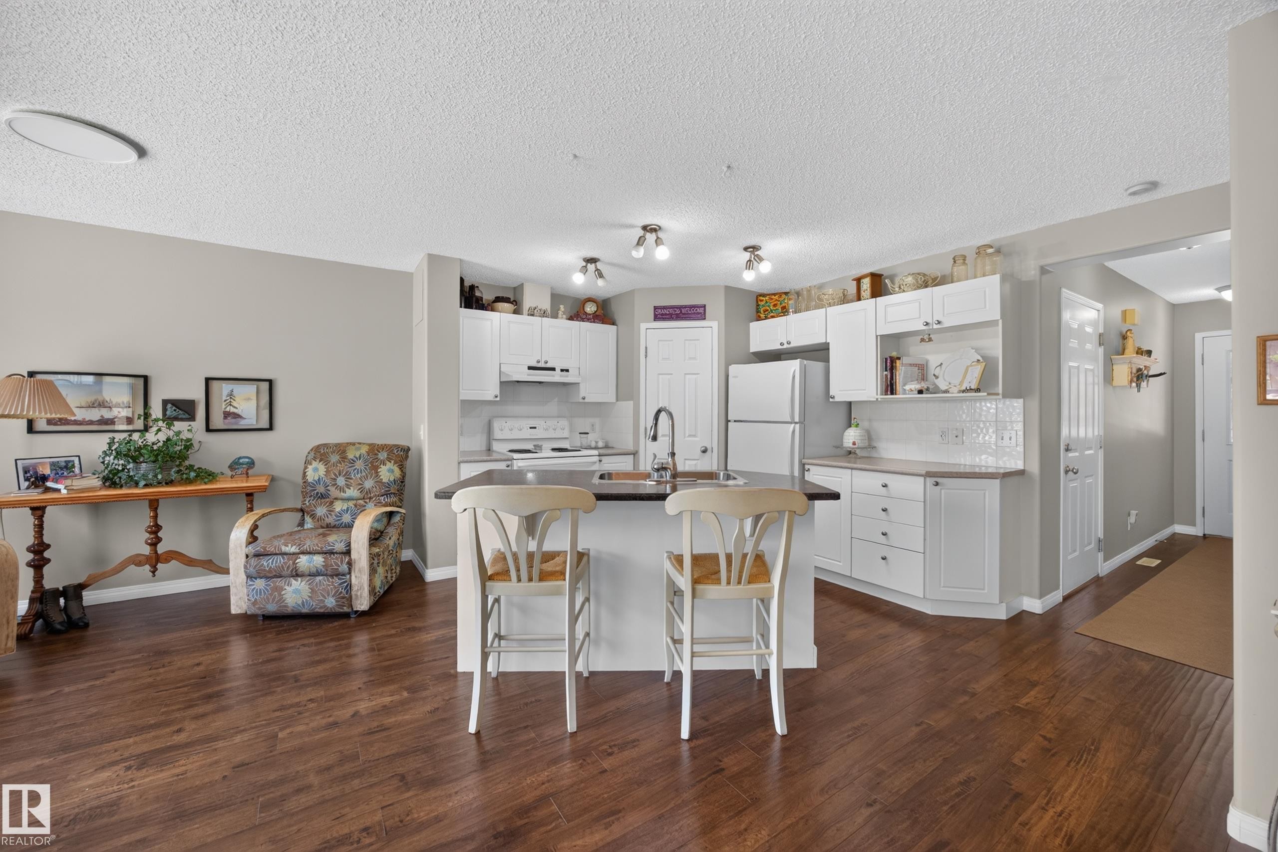 Open concept kitchen featuring white cabinetry, a kitchen island with seating, dark countertops, white subway tile backsplash, and stainless steel appliances - #7 155 Crocus Cr, Sherwood Park, AB - Indoor