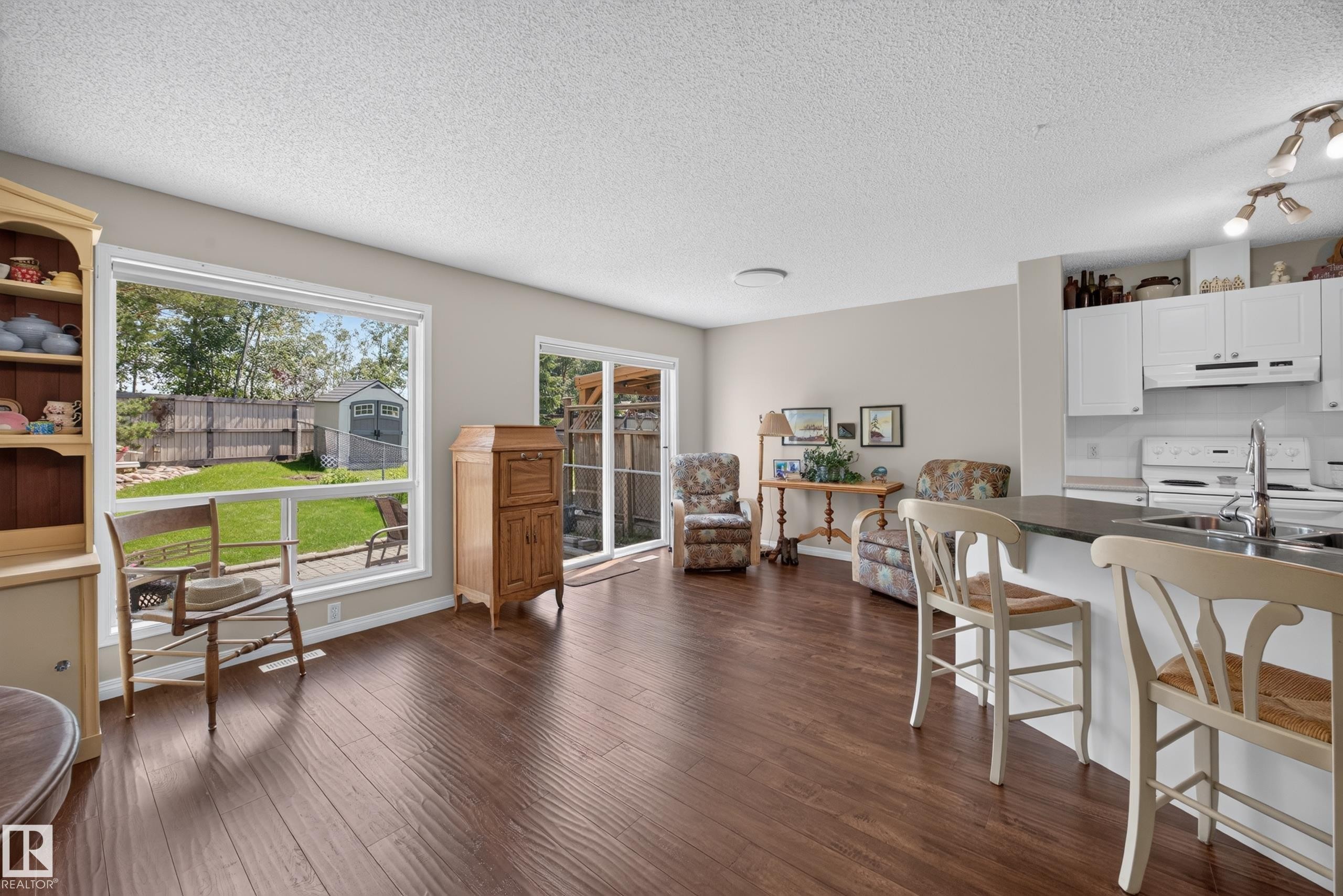 Open-concept living space featuring wood-finish flooring, a kitchen island with seating, white cabinetry, and a sliding glass door to the exterior - #7 155 Crocus Cr, Sherwood Park, AB - Indoor