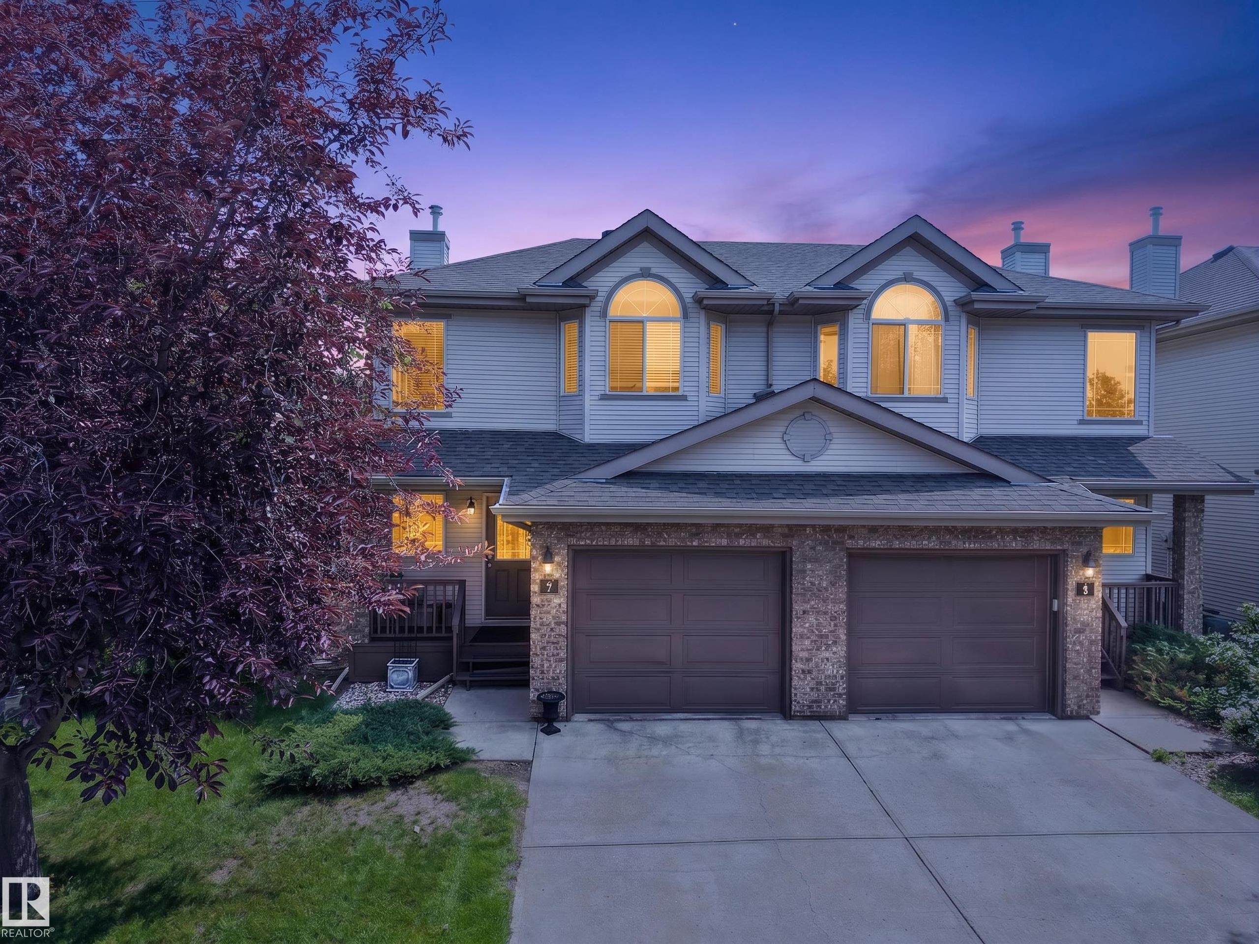 Two-story residence featuring light-colored siding, a two-car garage with brick-finish accents, and multiple dormer windows - #7 155 Crocus Cr, Sherwood Park, AB - Outdoor With Facade
