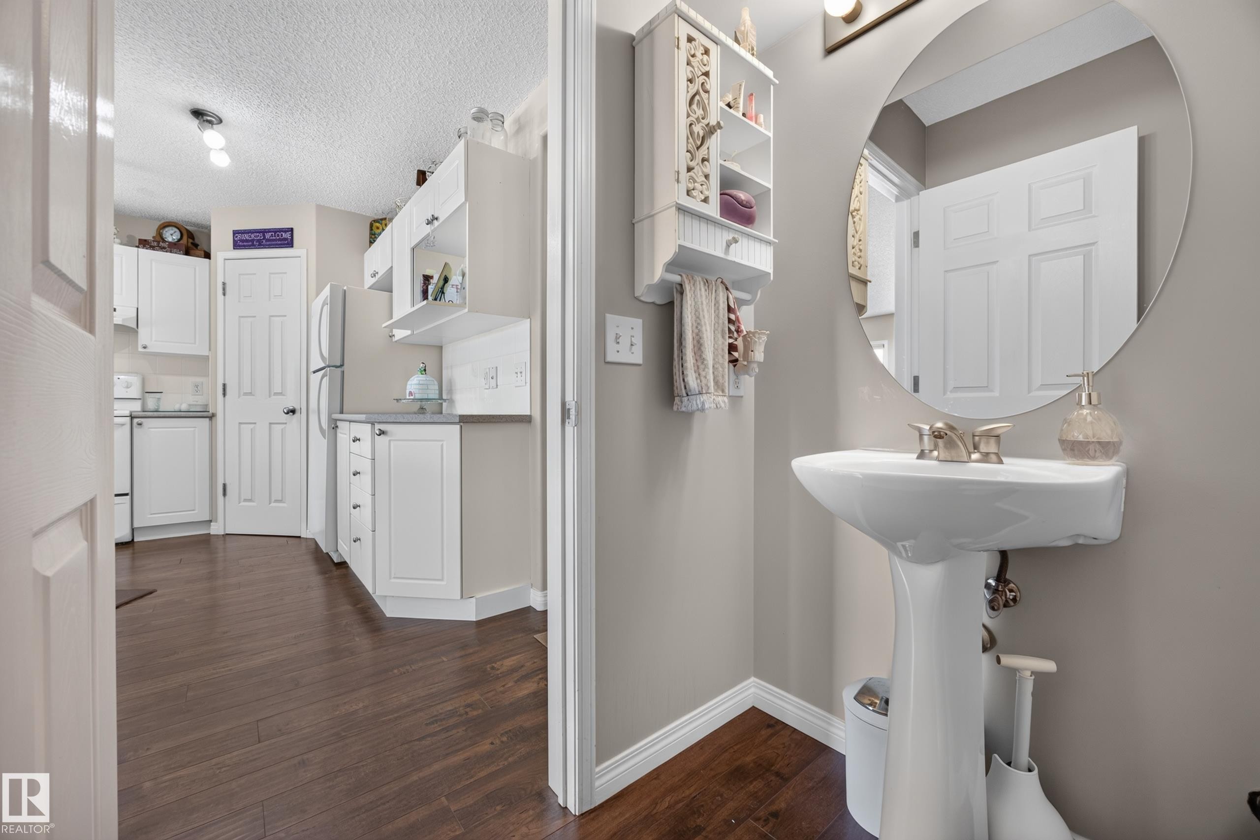 Pedestal sink with brushed nickel faucet, round mirror, and wood-finish flooring - #7 155 Crocus Cr, Sherwood Park, AB - Indoor Photo Showing Bathroom