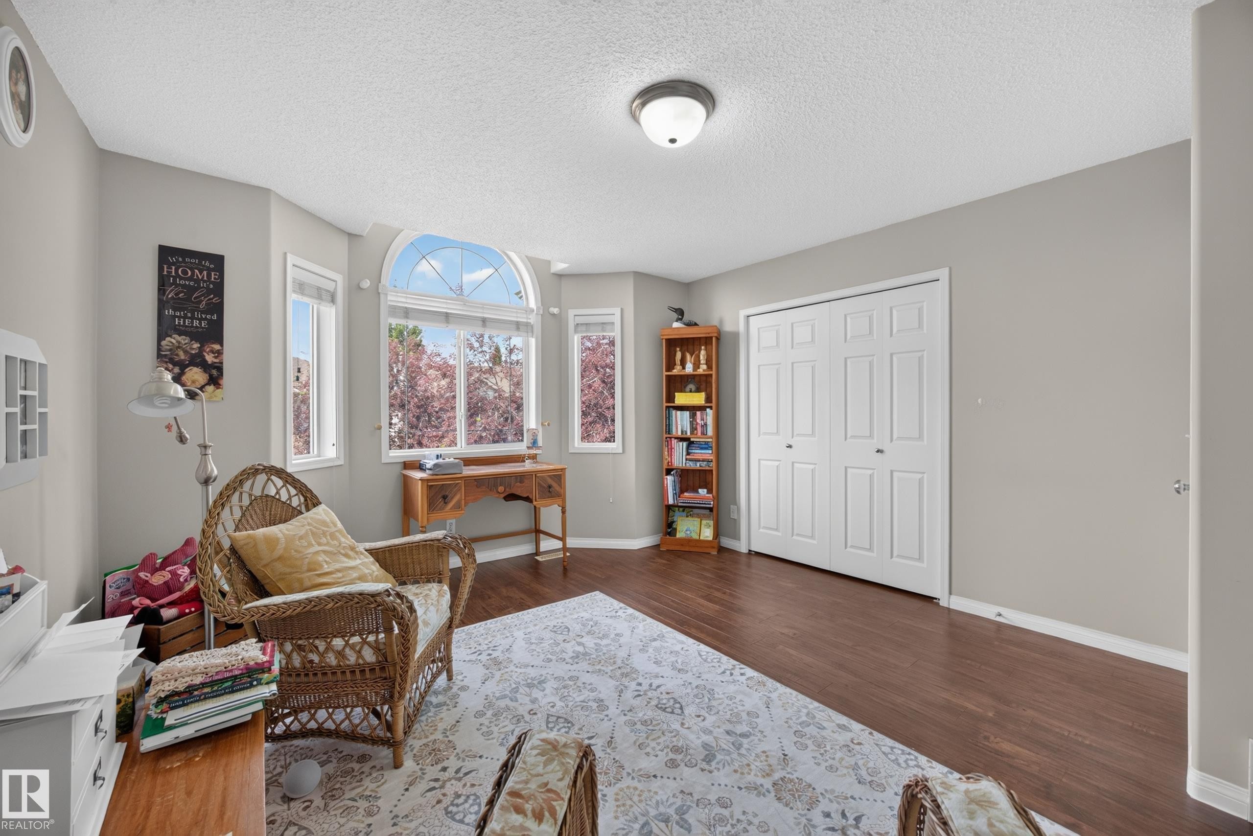 Spacious room featuring multiple windows including an arched transom window, wood-finish flooring, white bi-fold closet doors, and light gray wall paint - #7 155 Crocus Cr, Sherwood Park, AB - Indoor