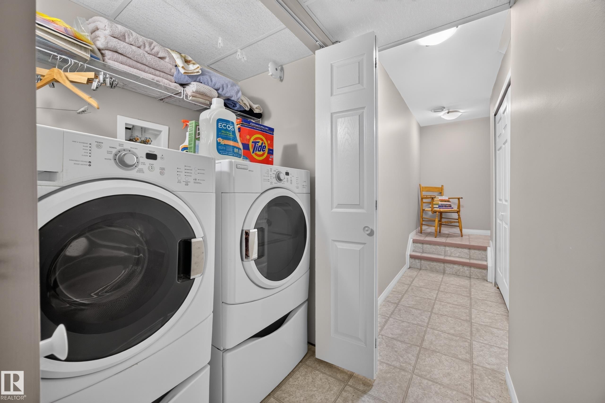 Dedicated laundry area featuring front-loading washer and dryer units, overhead wire shelving for storage, and light-toned wall paint - #7 155 Crocus Cr, Sherwood Park, AB - Indoor Photo Showing Laundry Room
