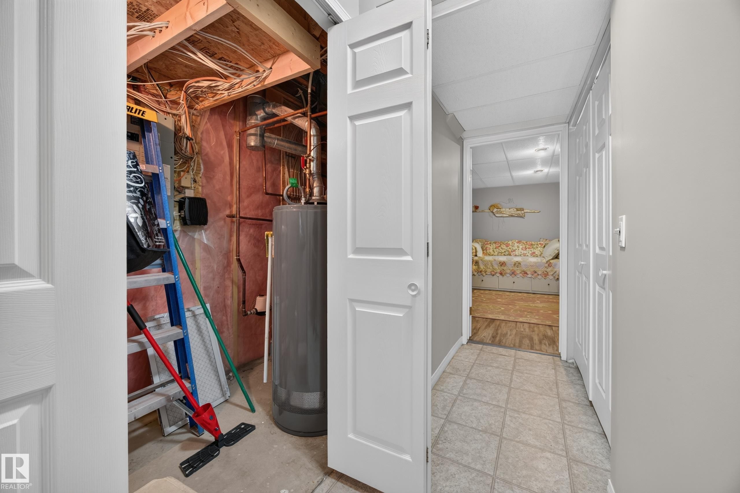 Basement utility area featuring exposed wood joists and a water heater, with a separate finished area showing wood-finish flooring - #7 155 Crocus Cr, Sherwood Park, AB - Indoor Photo Showing Other Room
