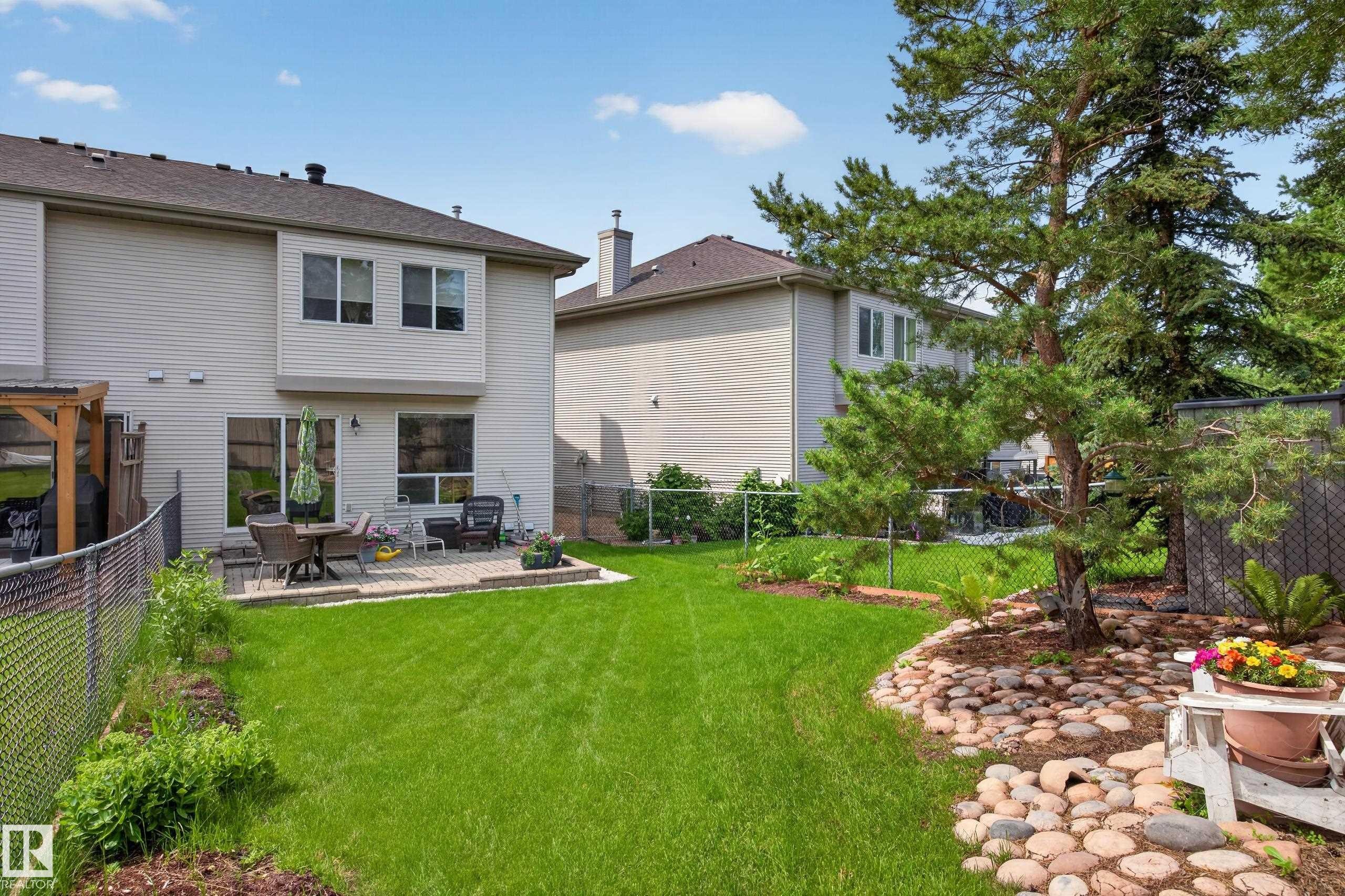 Expansive backyard featuring a large green lawn, a stone patio, and mature trees - #7 155 Crocus Cr, Sherwood Park, AB - Outdoor With Backyard With Exterior