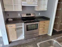 Stainless steel electric range with overhead exhaust hood, wood-finish cabinetry, dark speckled countertops, and tile flooring -