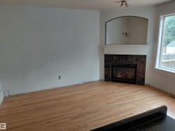 Light wood-finish flooring, corner fireplace with dark tile surround, integrated arched alcove, and white mantel -