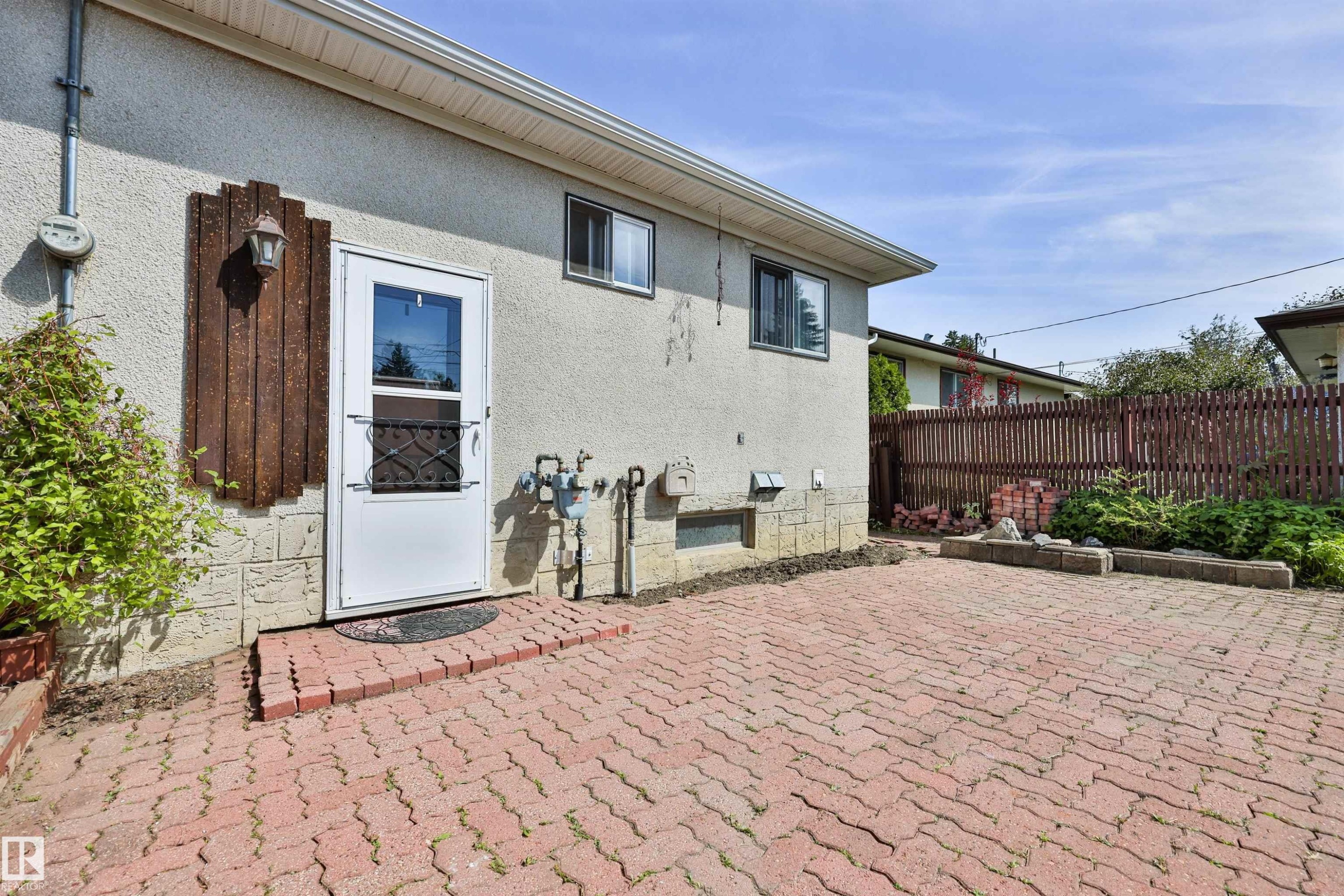 Exterior featuring a white entry door with security screen, concrete stucco siding, and a red brick paver patio - 3824 111B Street Nw, Edmonton, AB - Outdoor With Exterior
